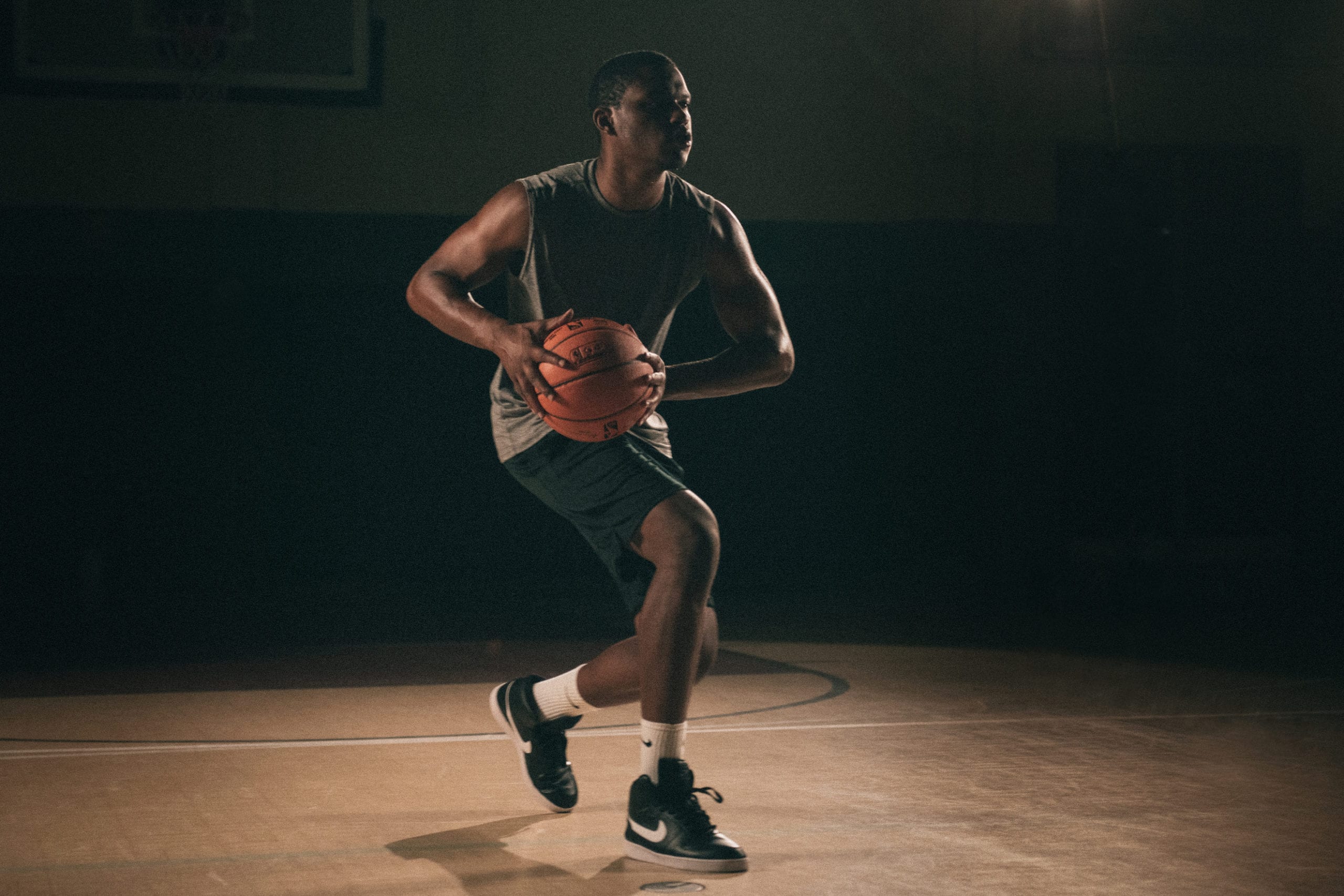 Creative Marketing Concept for Nike Sneakers An African American man poised holding a basketball on a basketball court with a light shining on him in semi darkness