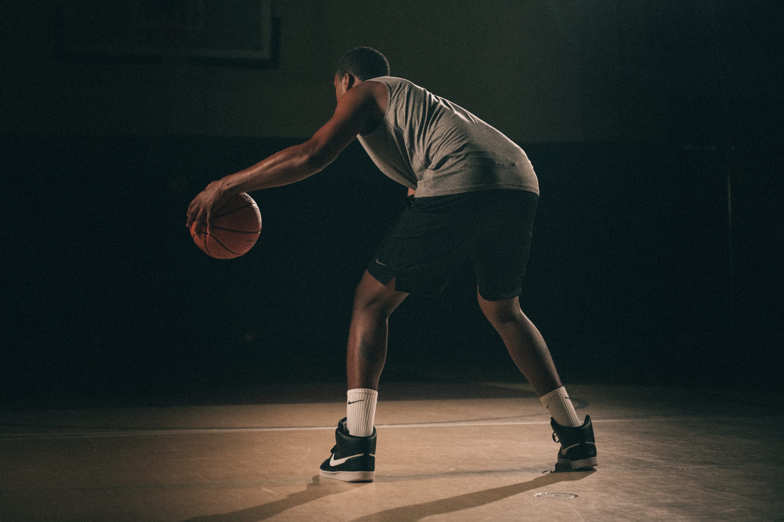 Nike Creative Marketing Concepts View from behind of an African American man poised holding a basketball on a basketball court with a light shining on him in semi darkness