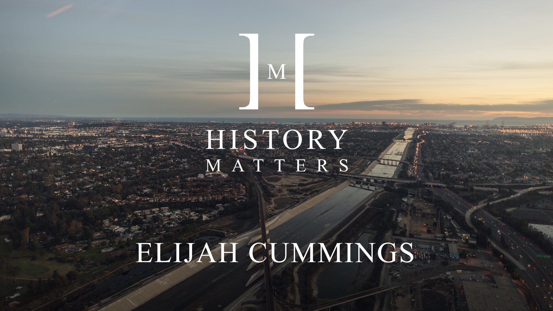 White HM Elijah Cummings logo with background aerial view of city with bridges crossing a waterway