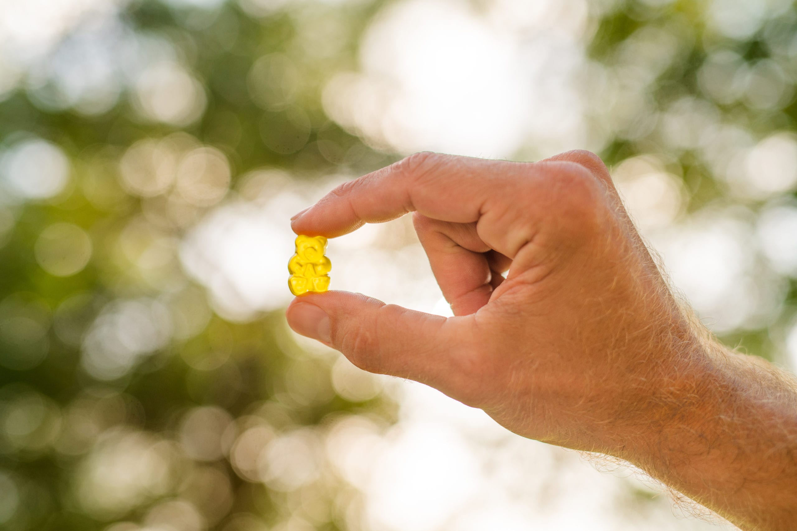 JustCBD Product Photography and Just CBD Products Man holding yellow gummy bear between thumb and forefinger