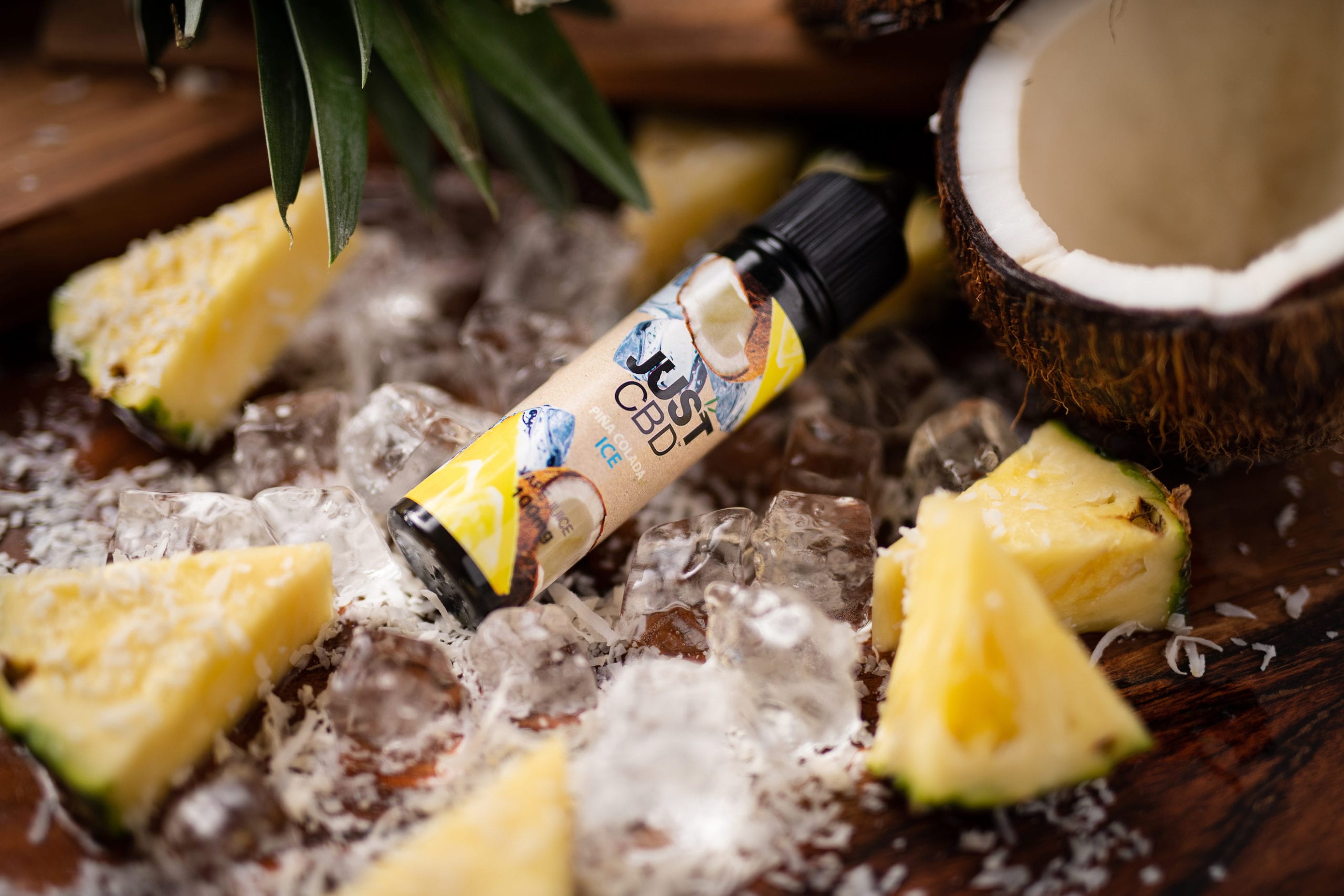 IU C&I Studios Portfolio and Page JustCBD Product Photography and Just CBD Products Pina Colada ICE vape juice container on display surrounded with chunks of pineapple and coconut