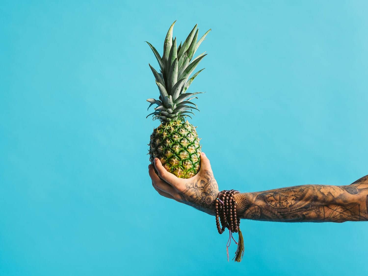 Tattooed arm wearing bracelets holding a pineapple