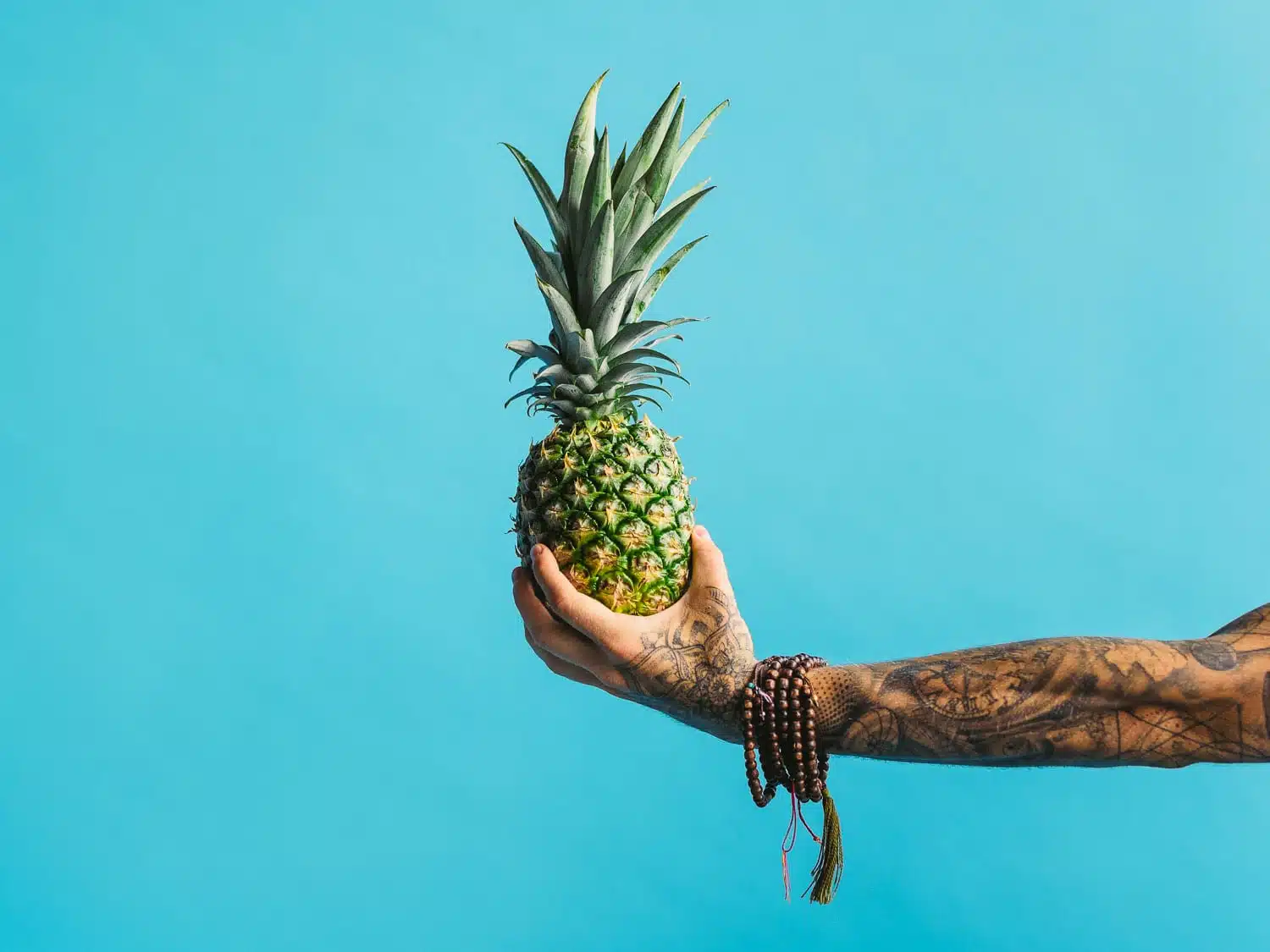 Buddha Bowl 7 Tattooed arm wearing bracelets holding a pineapple