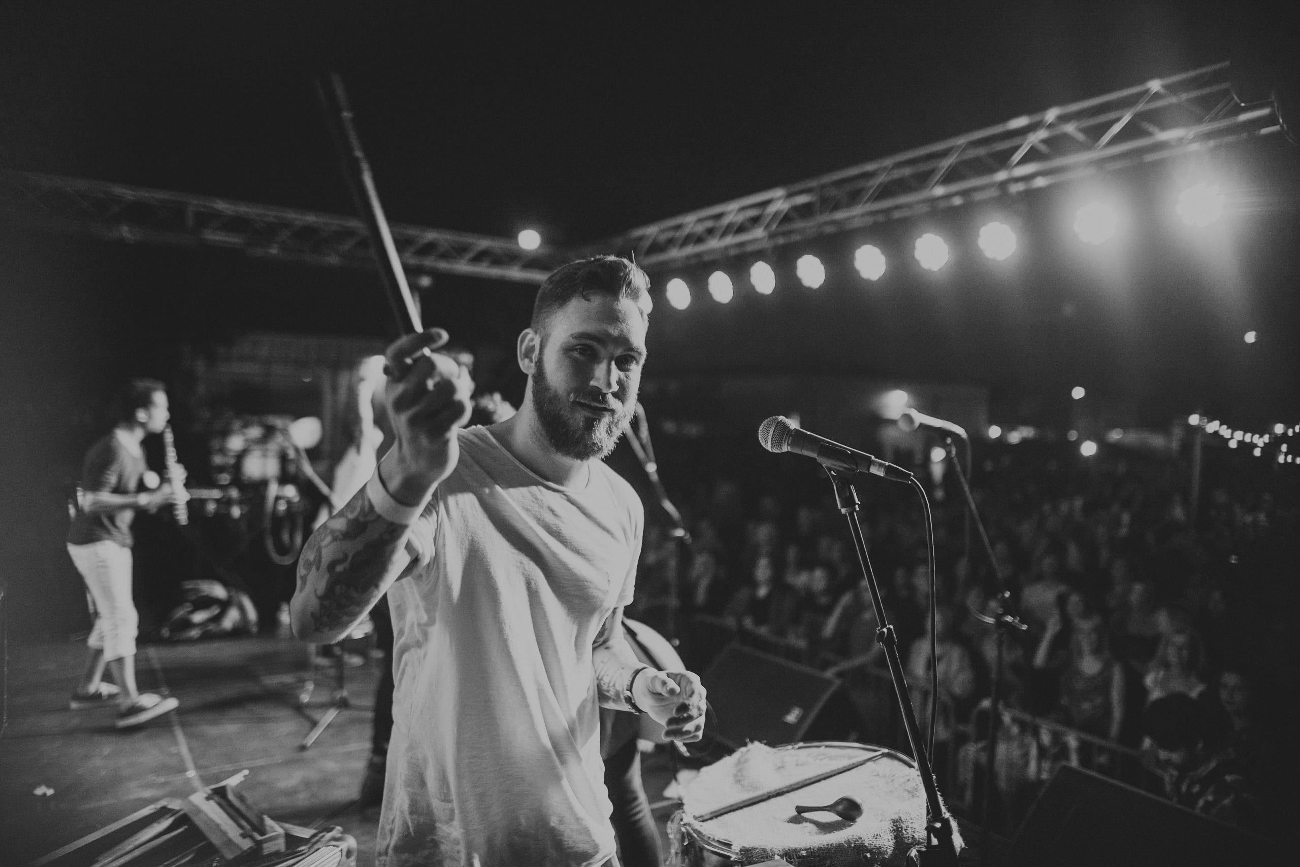 Black and white of a short haired with a beard flute player posing for the camera holding the flute in his hand in front of an audience