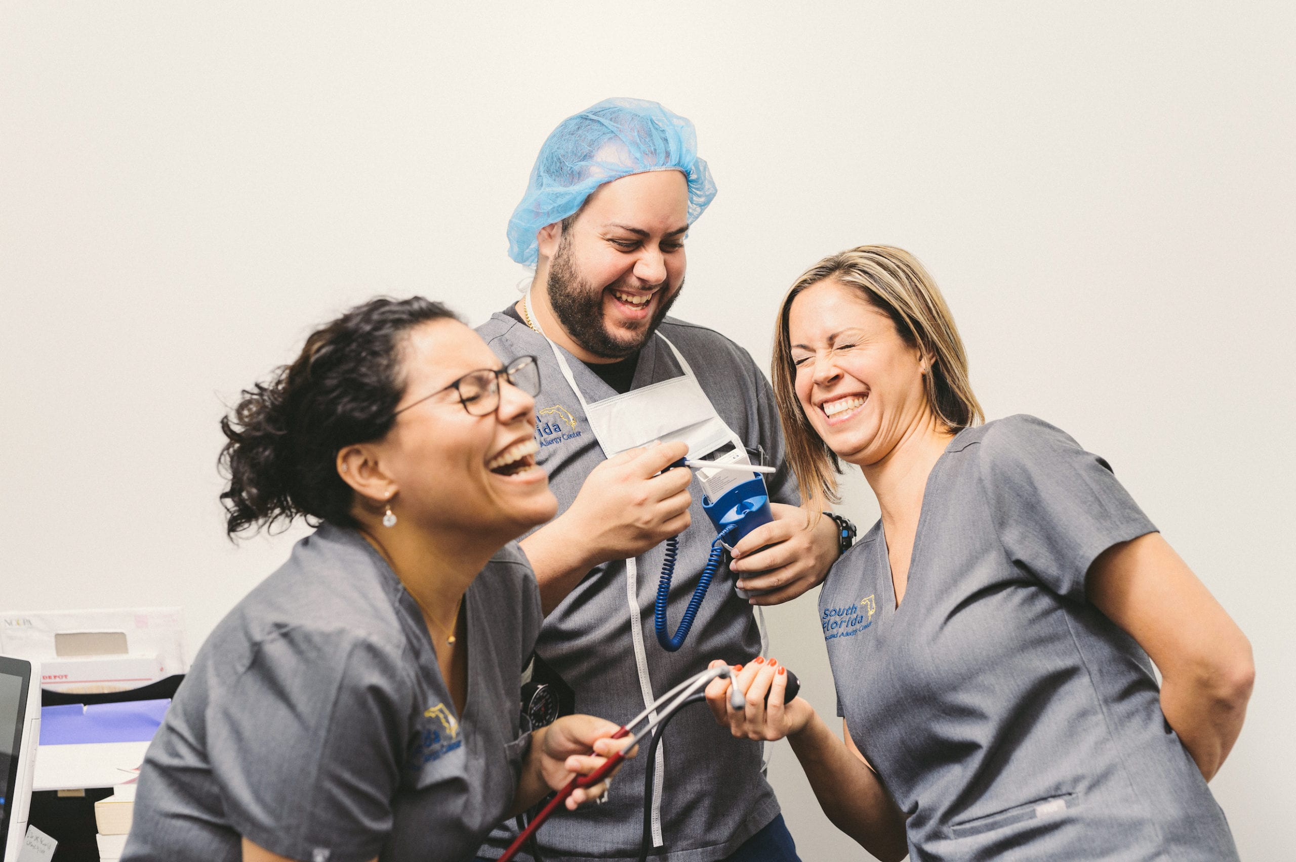 Two female doctors holding a stethoscope and one male doctor holding a thermometer sharing a laugh