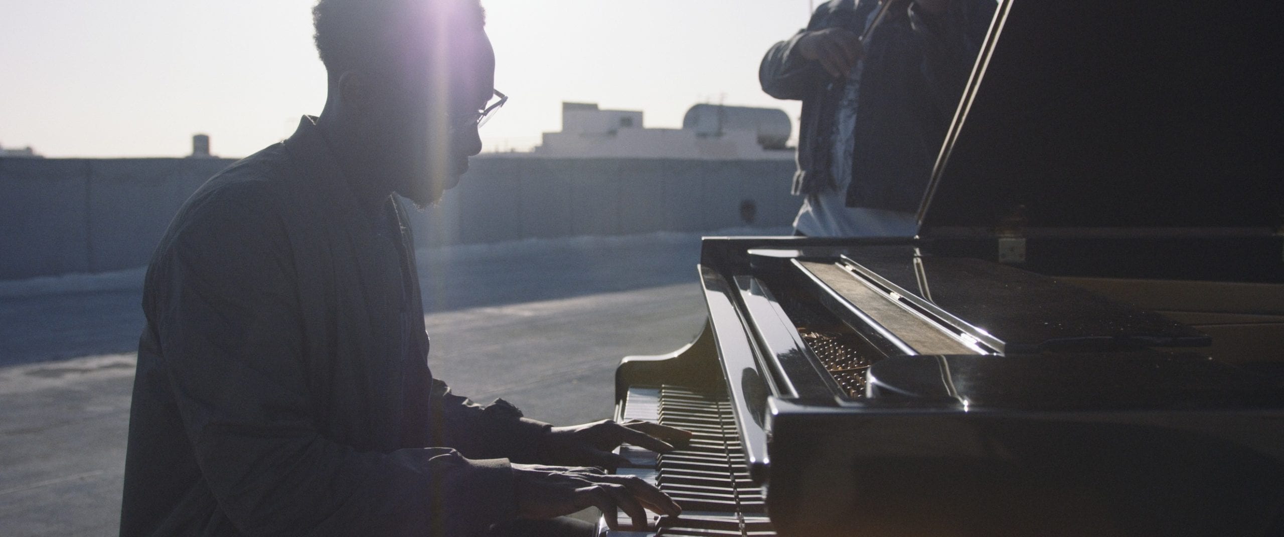 Black Violin One Step Music Video Side profile of a man wearing glasses playing a piano on a concrete rooftop