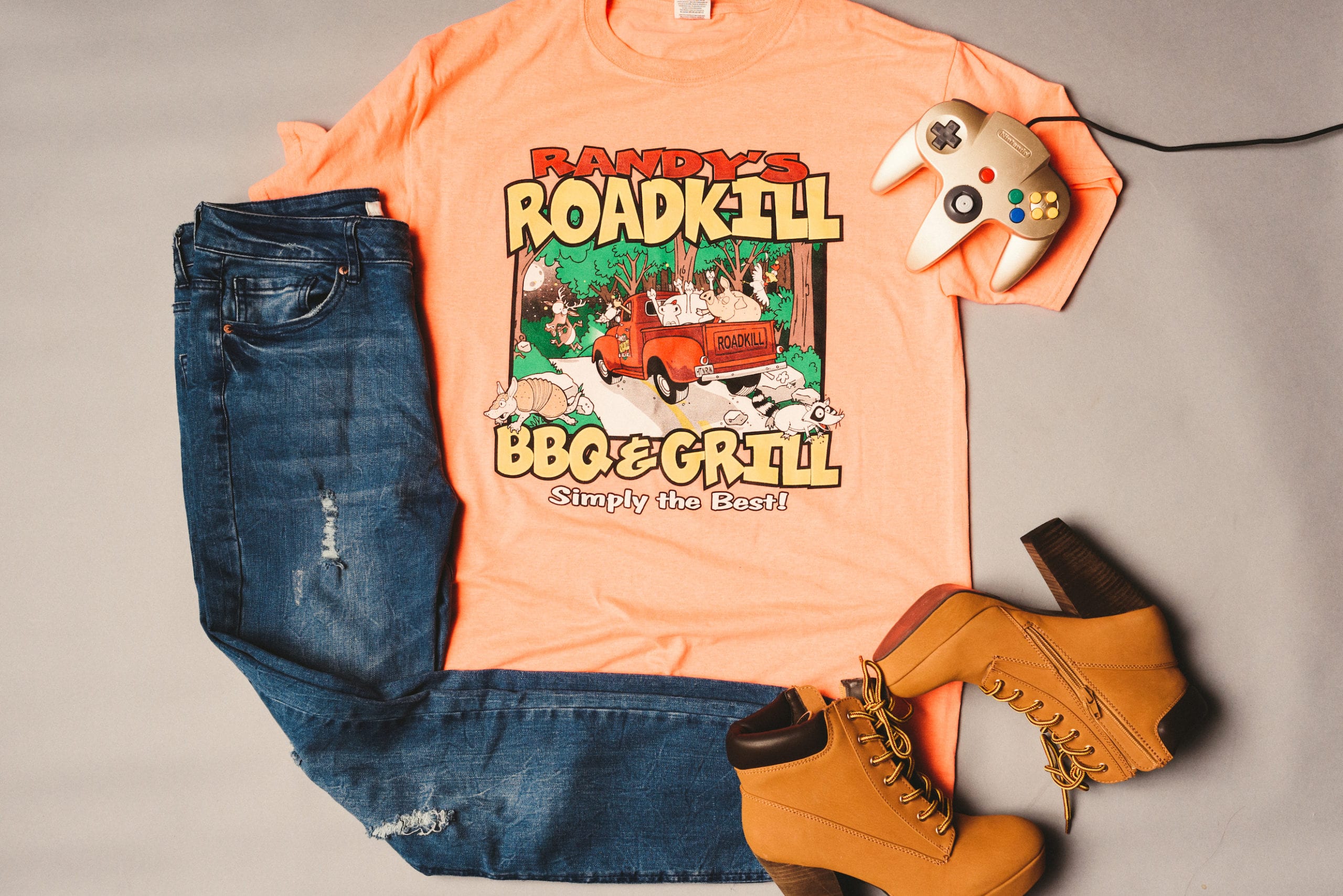 IU C&I Studios Portfolio Heart Piece Media Day Orange Randy's Roadkill BBQ & Grill t shirt with jeans and leather high heel boots along with Nintendo controller on display