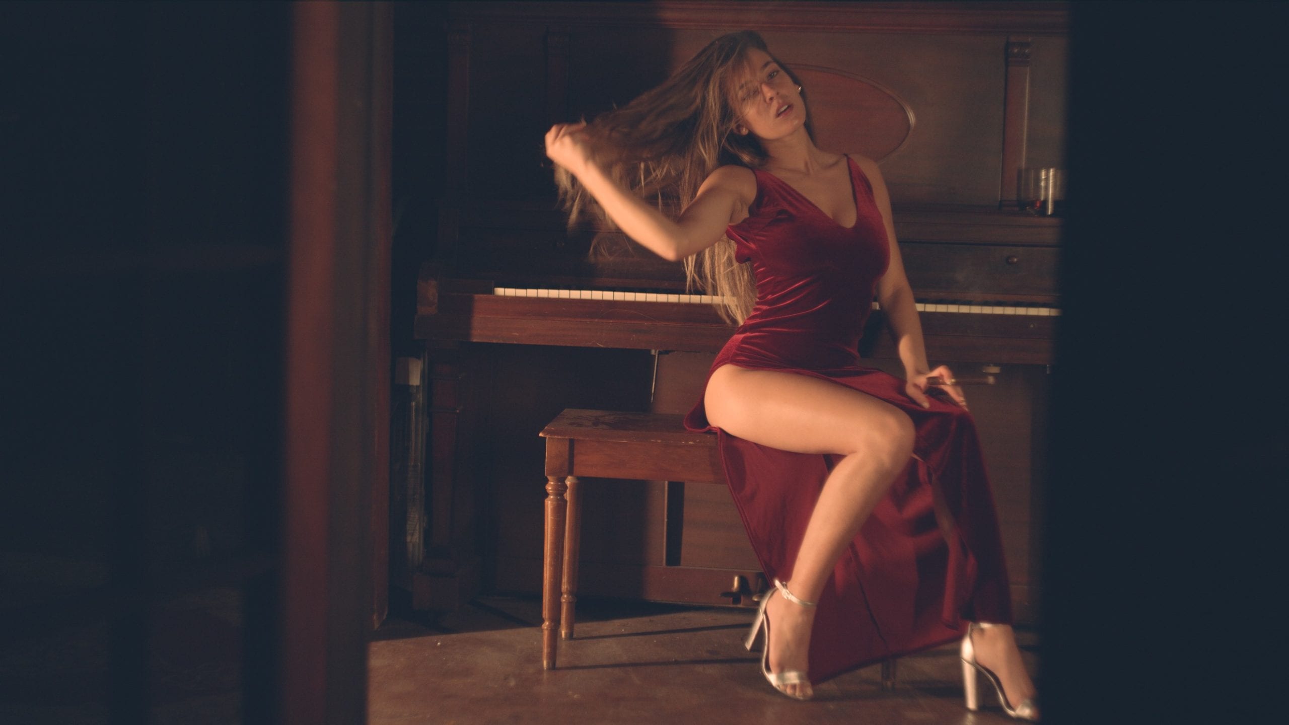 Sabela Model posing for camera sitting at a piano wearing a red dress holding a cigar and high heels