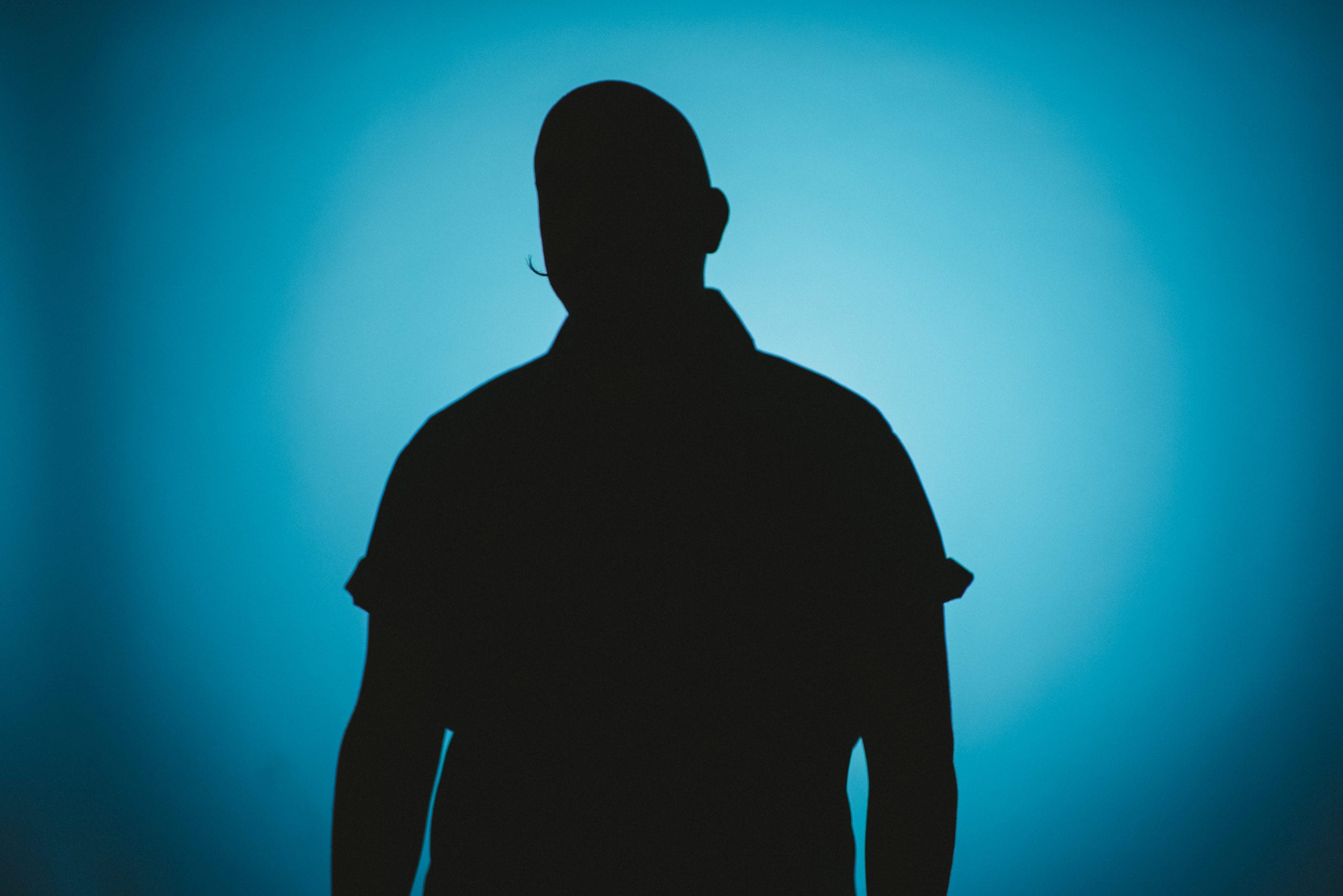 Silhouette of a bald man wearing a moustache posing for the camera with a light blue background