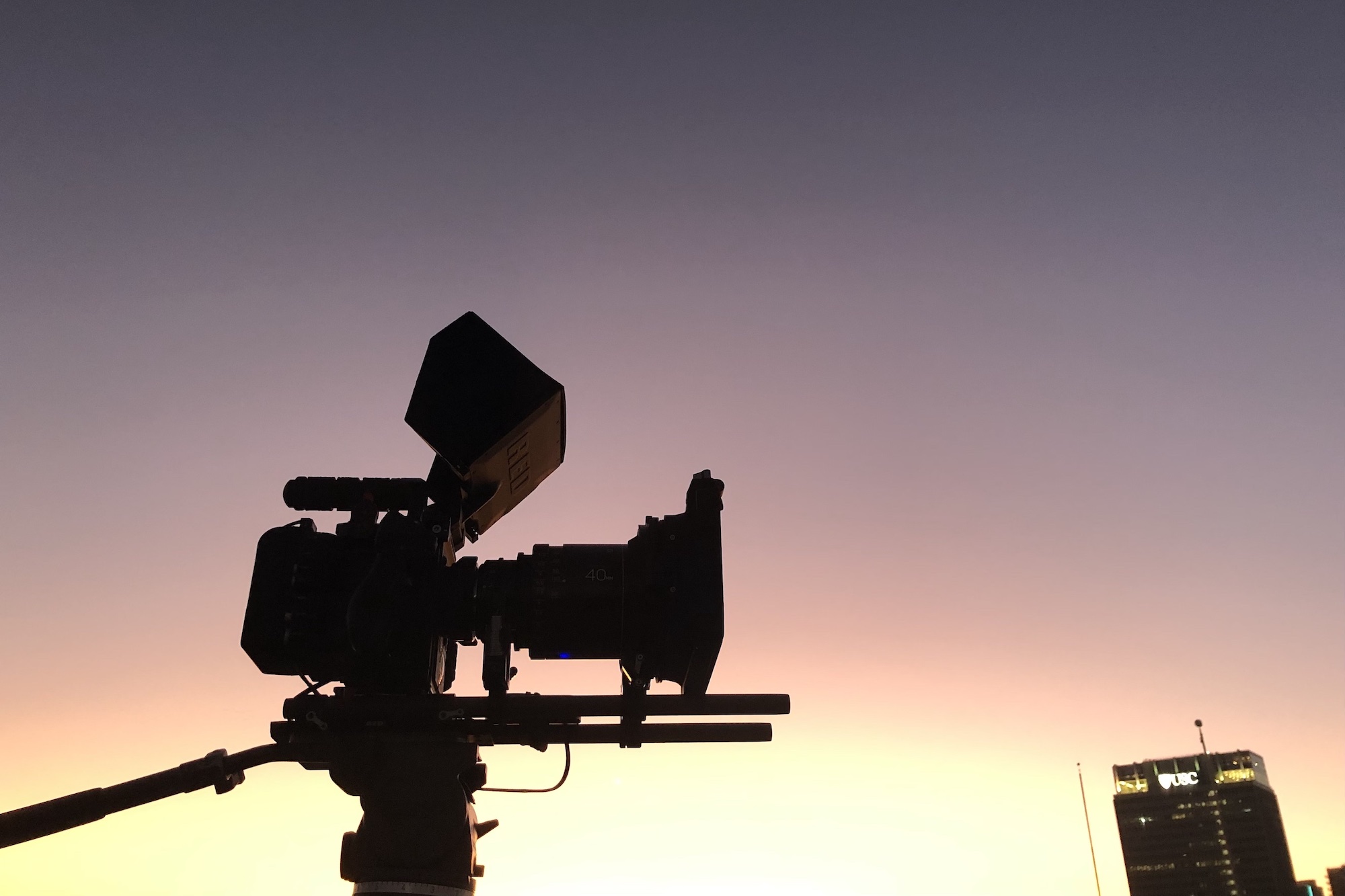 Black Violin BTS Side view showing silhouette of video camera at dusk with building in the background