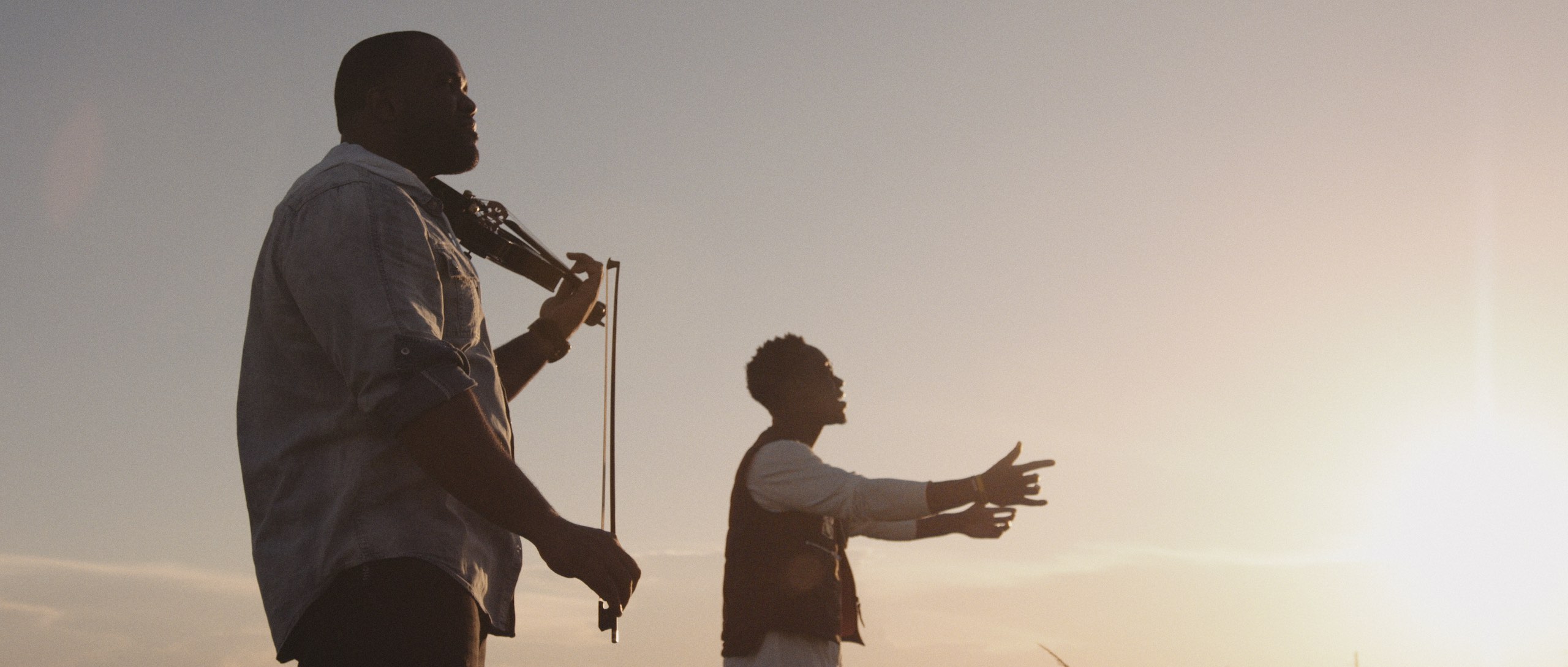 Closeup side profile of man playing violin with another man singing next to him