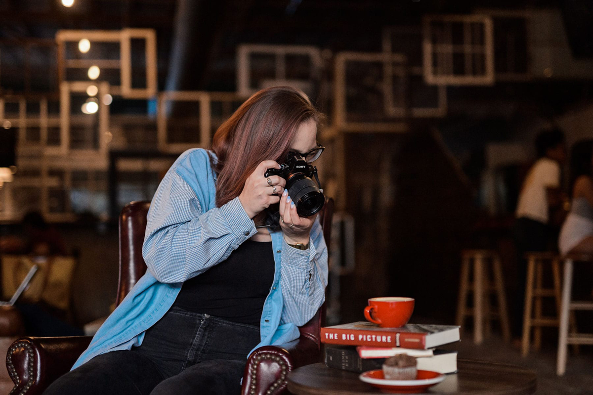 Woman taking picture of muffin on table with books and red coffee cup