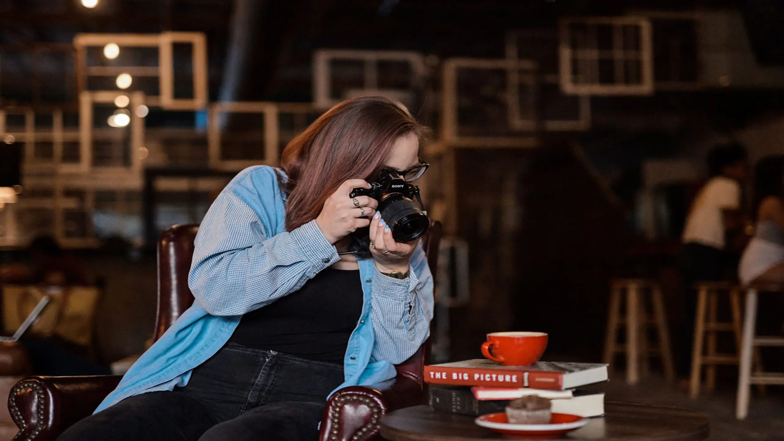 post-4-definitive-reasons-why-creative-product-photography-sells6 Woman taking picture of muffin on table with books and red coffee cup