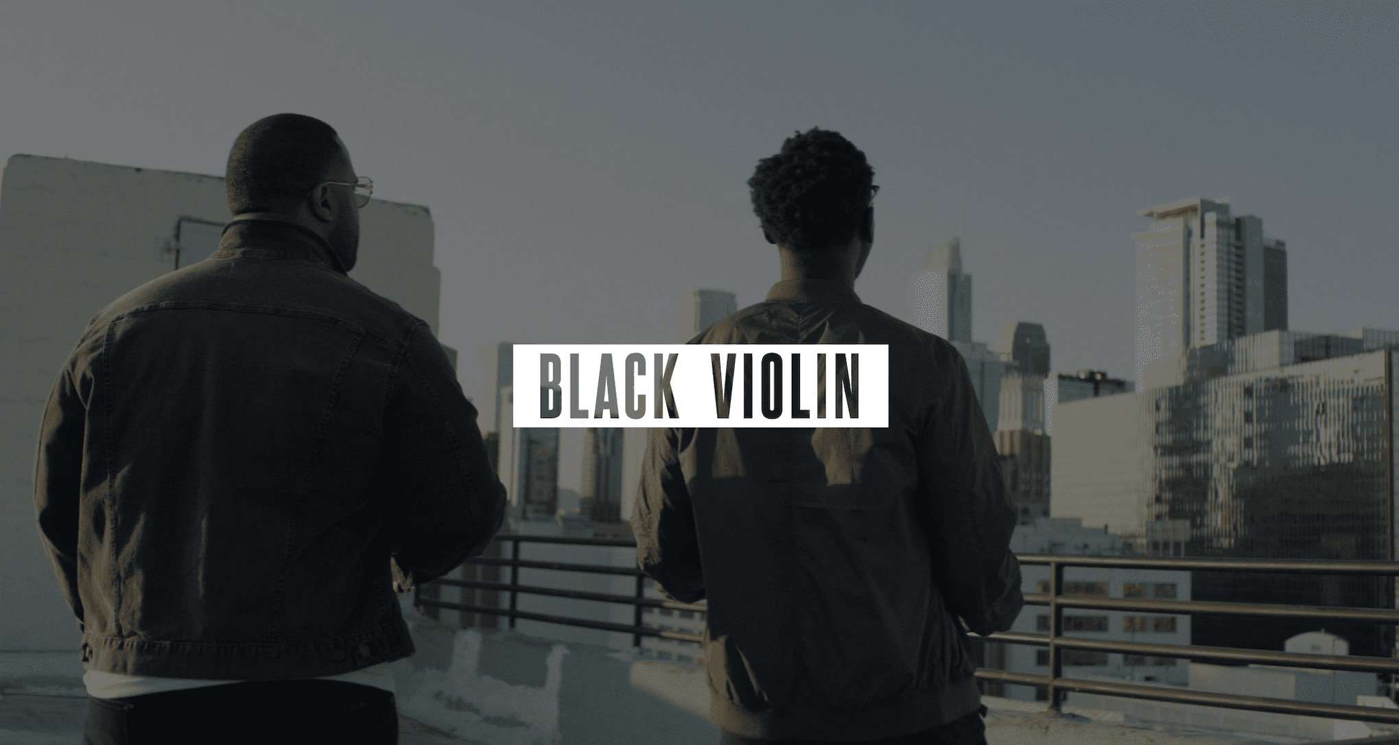 Audio Services by C&I Studios Video Production Services to Podcast Recording Studio Gray Black Violin logo on white against a dimmed background of two men standing on a concrete rooftop looking out over the city