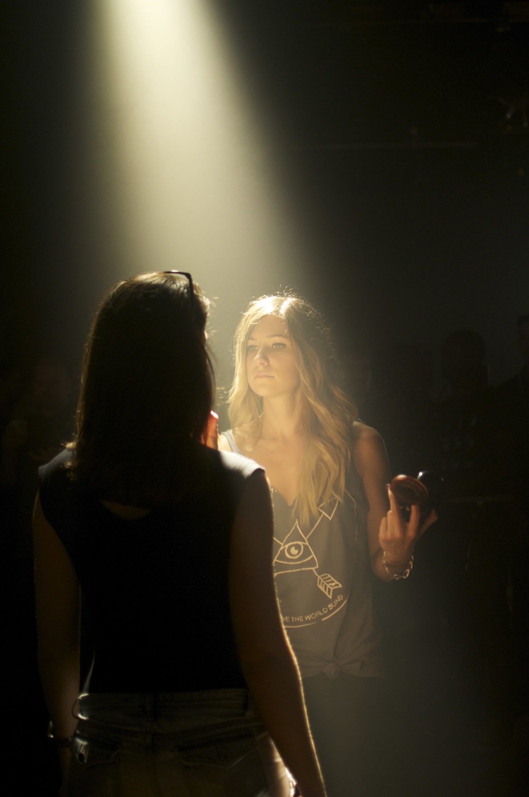 Makeup artist with long blond hair applying makeup to a model in a studio with a yellowish light shining on them