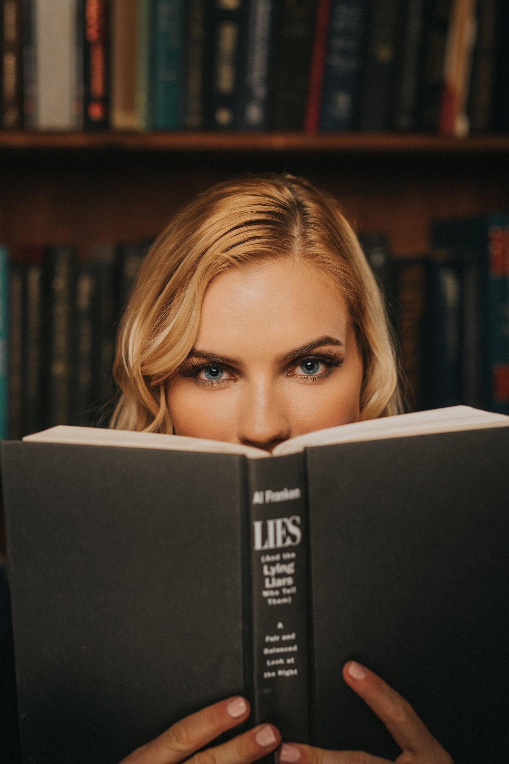 Professional Photography Services by C&I Studios Woman with blond hair posing for camera from behind a book
