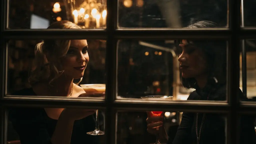 Two women looking out of a window while enjoying cocktails