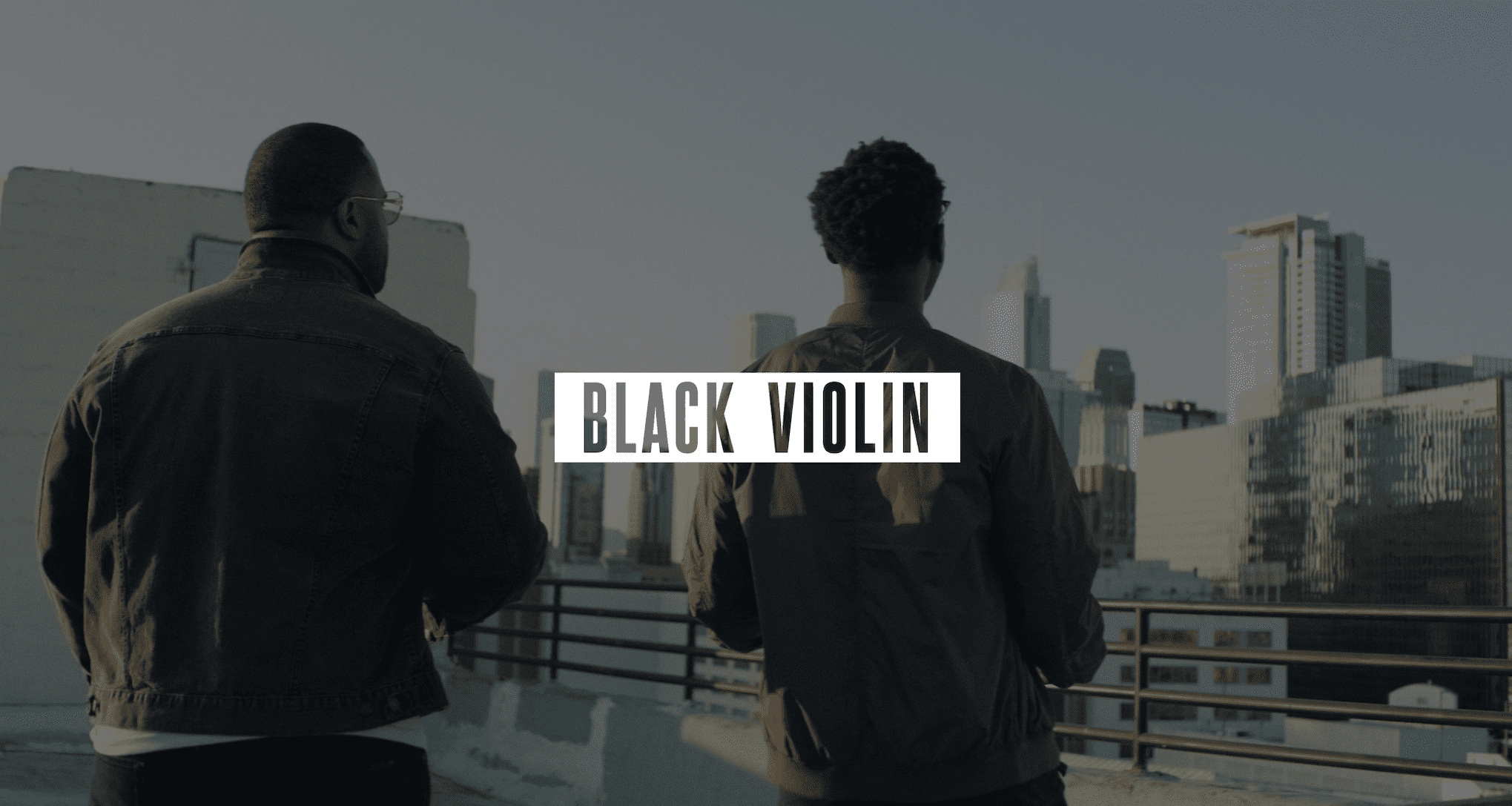 Keyword: Artist Management Services .Video Production Services to Podcast Recording Studio Gray Black Violin logo on white against a dimmed background of two men standing on a concrete rooftop looking out over the city