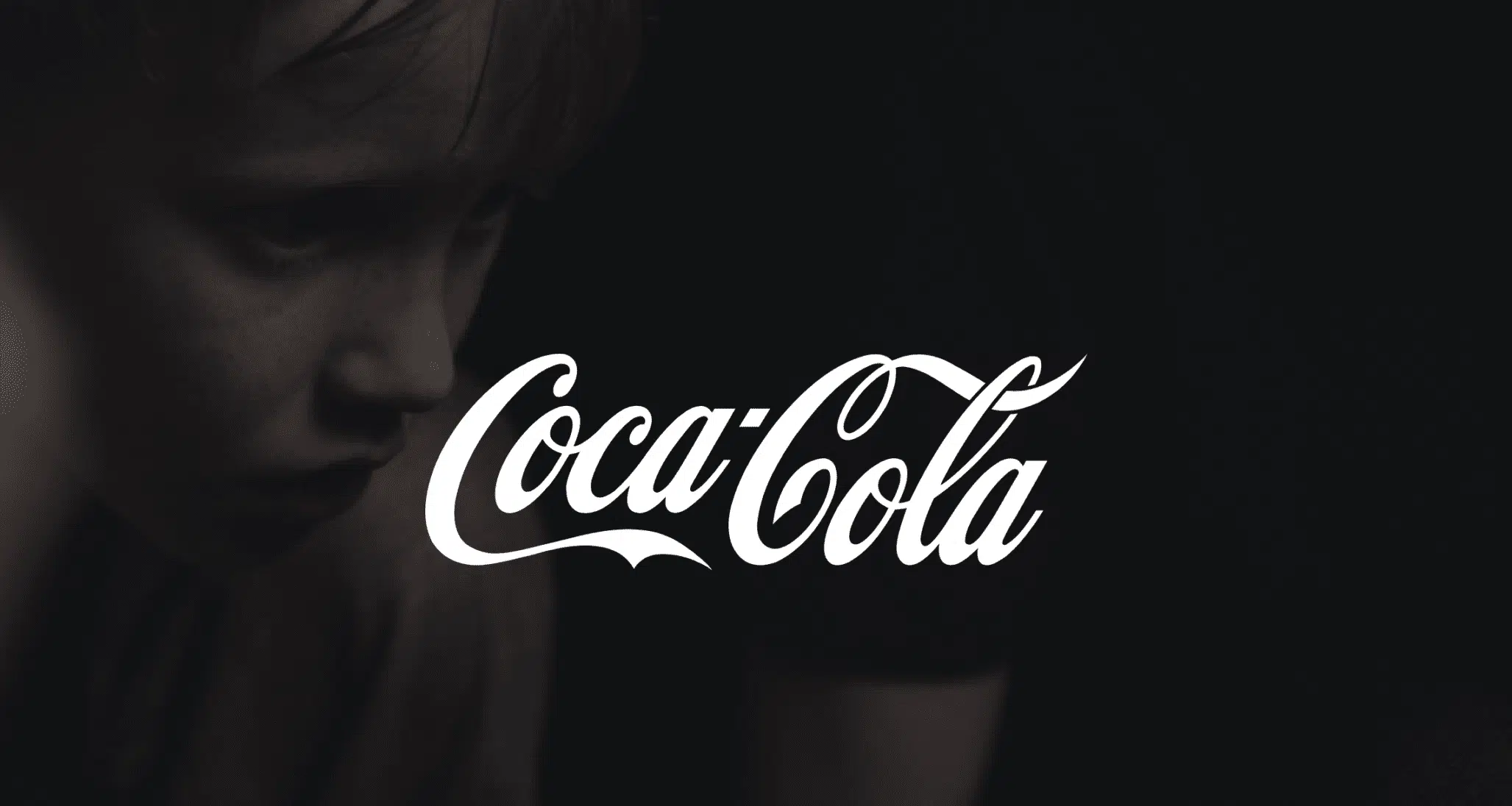 White Coca Cola logo against a dim background of a boy with freckles. Video Production Services