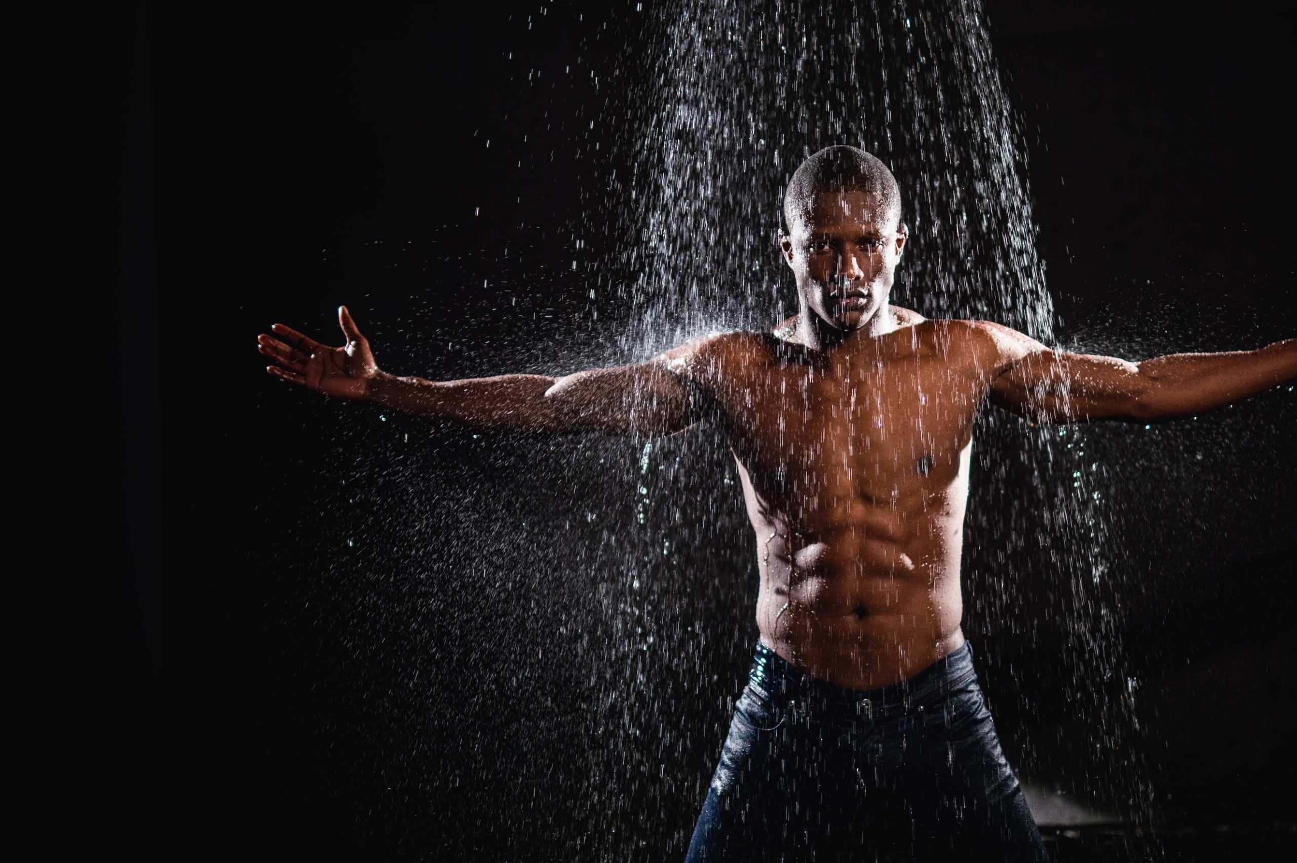 Crew Call Rain and Water Man with abs posing standing with arms outstretched to the sides under a shower of water