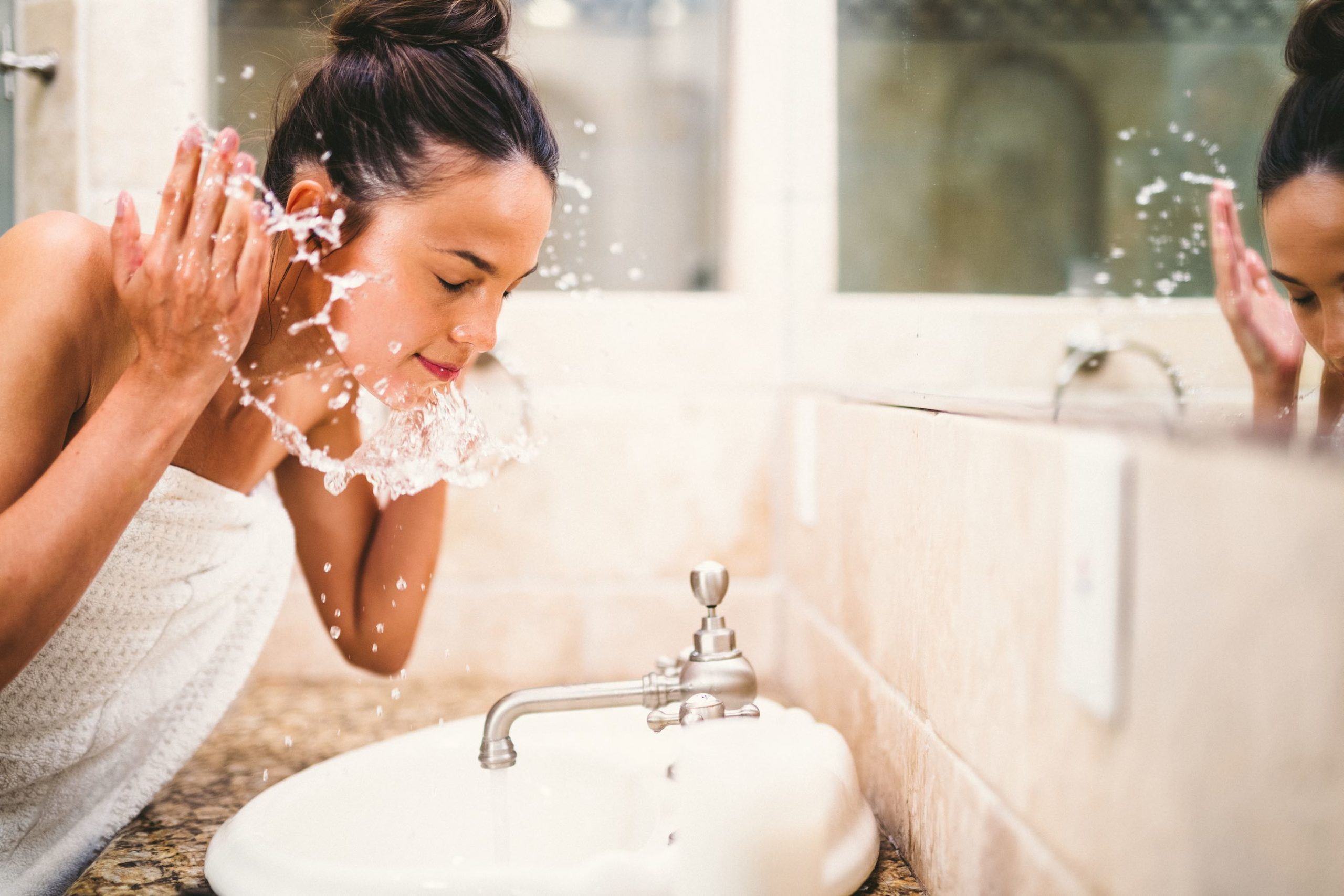 CBD Product Photography Laguna Blends Woman splashing water on her face by a sink with a mirror showing her reflection