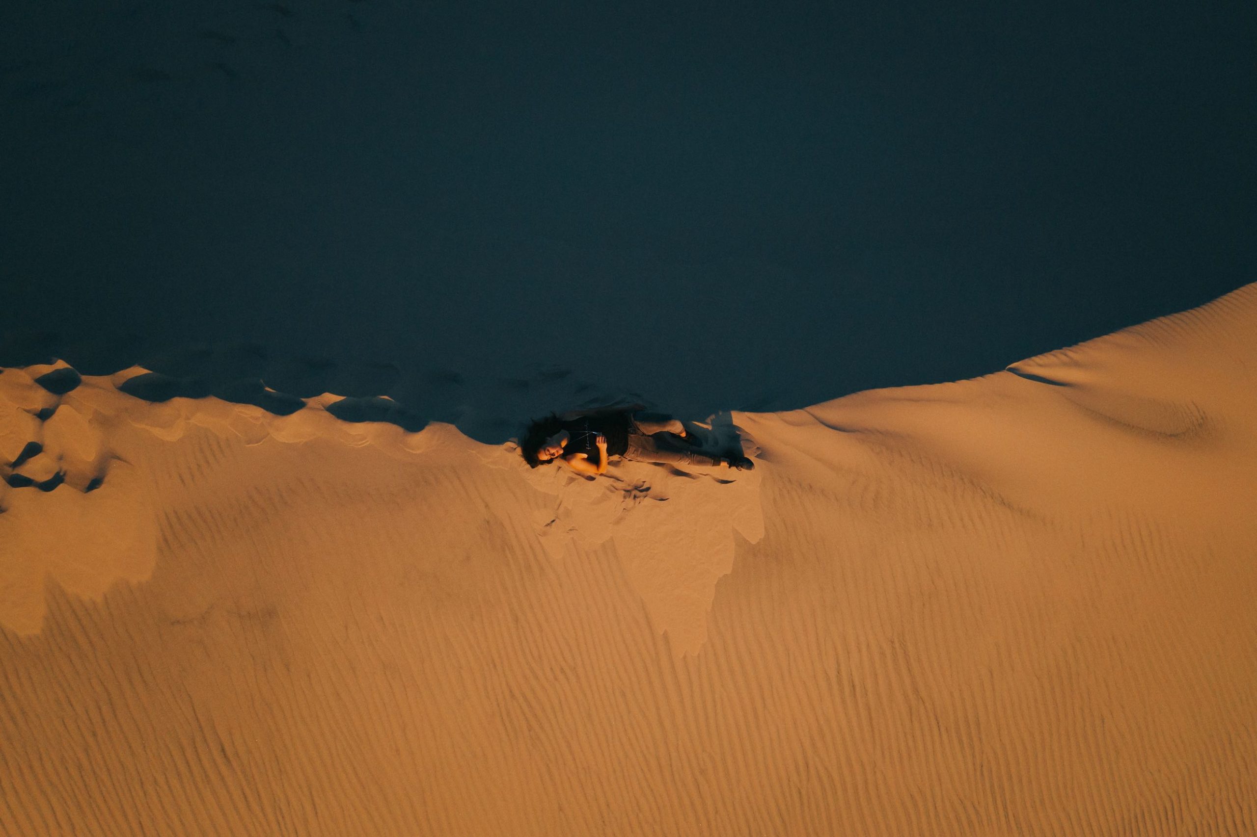 Komuso Design Photography Aerial view of a woman laying on a sand cliff holding a whistle she is wearing around her neck