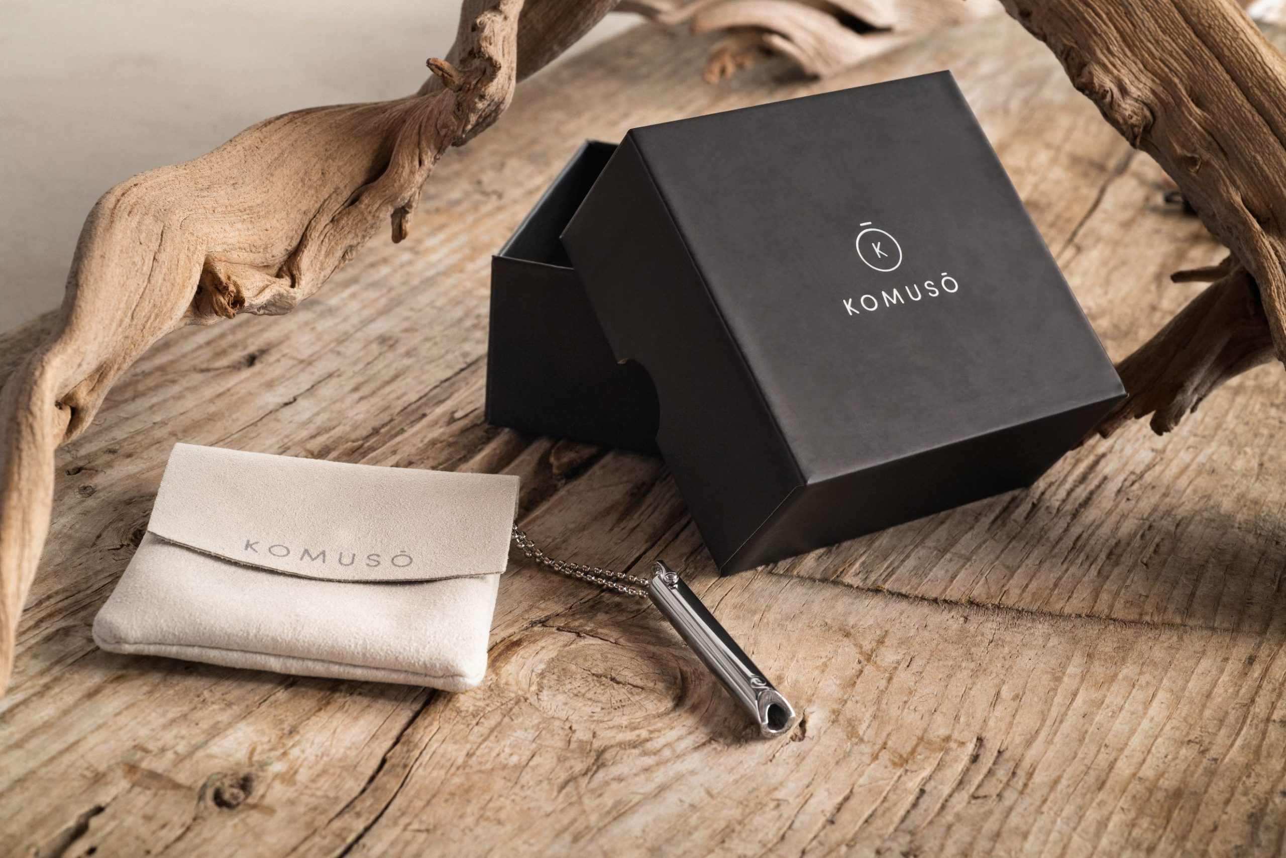 Komuso Design Photography Display of silver colored whistle, beige pouch and black box on a wooden table