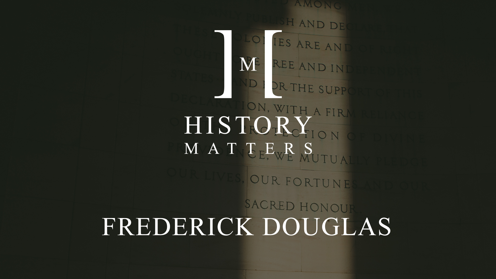 White HM Frederick Douglas logo with background of text on a stone wall