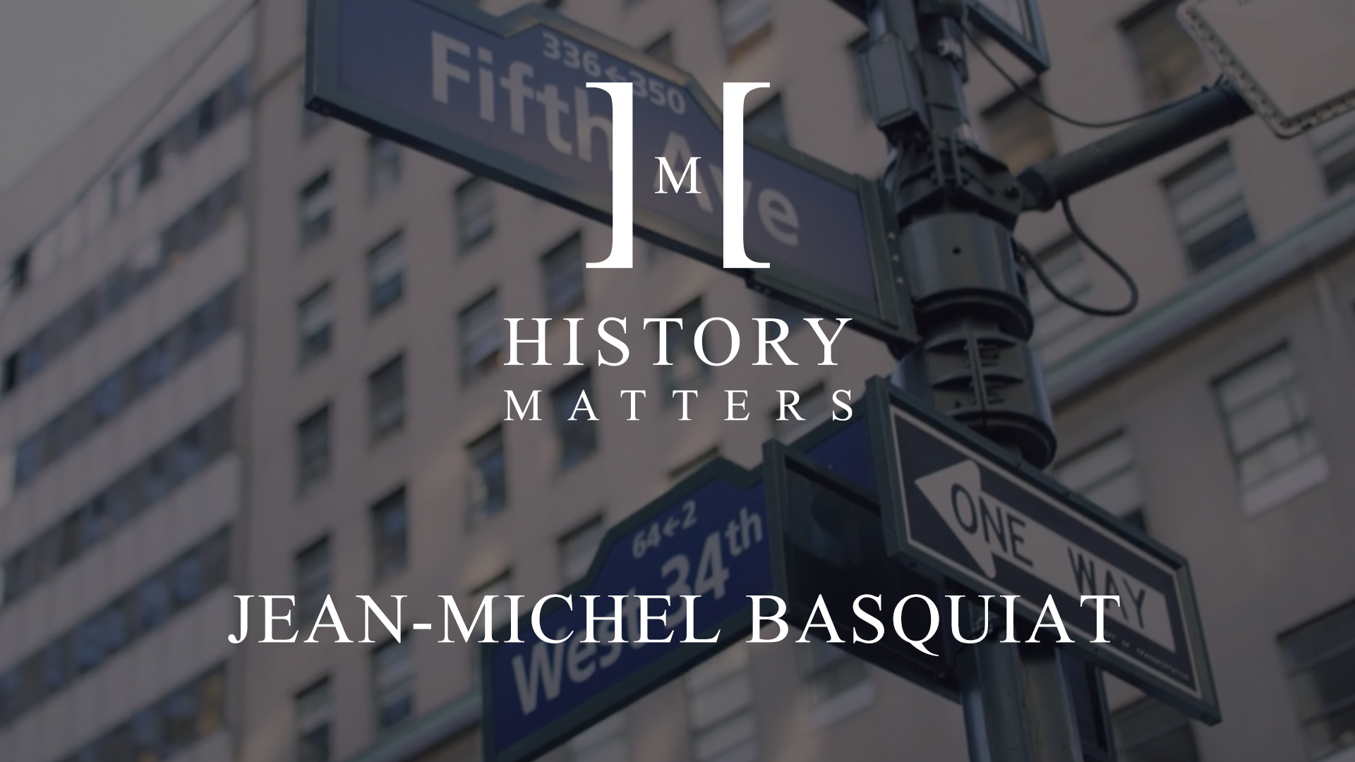 White HM Jean Michel Basquiat logo with dimmed background of West 34th and Fifth Avenue signs at intersection in New York City