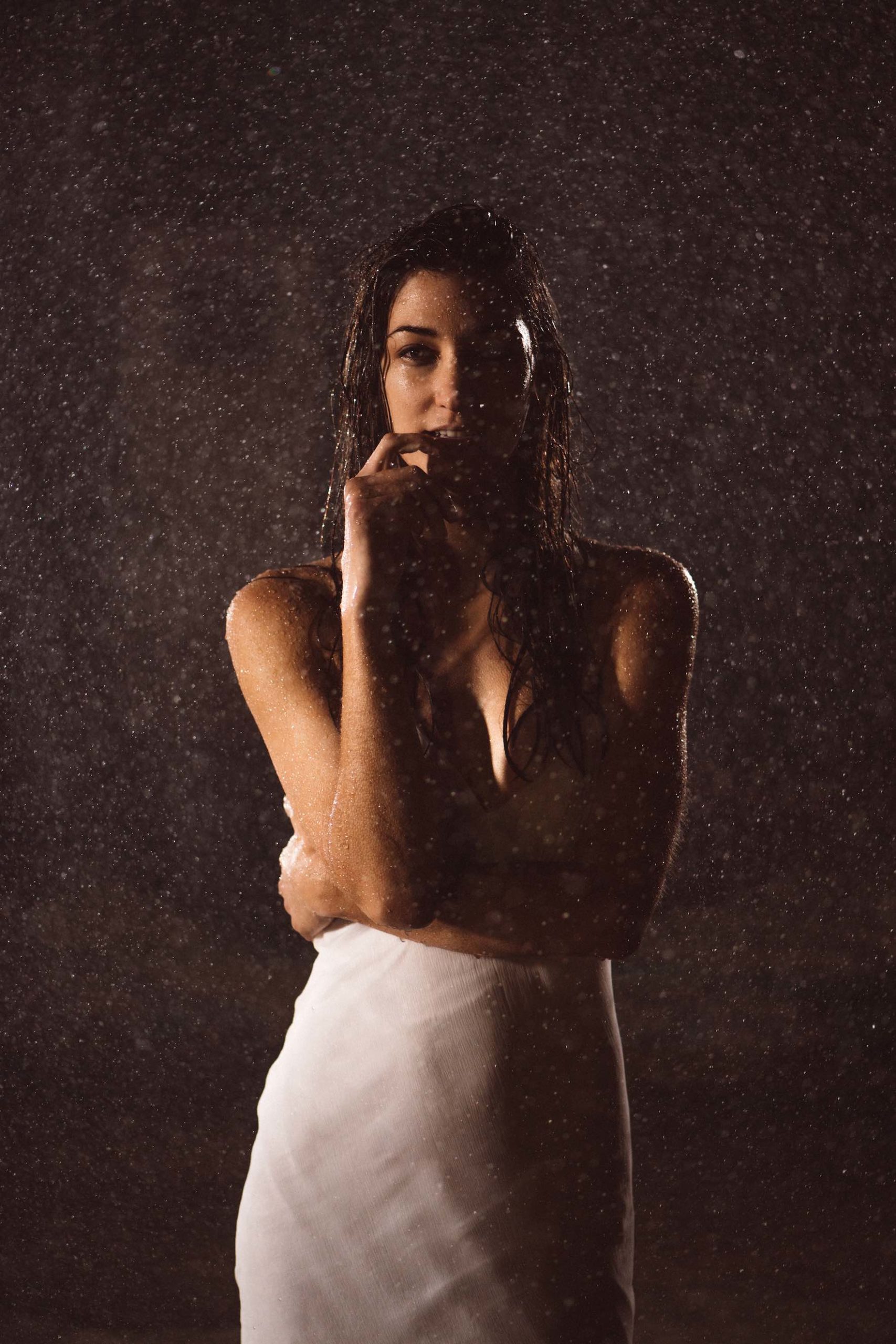 Crew Call Rain and Water Woman with long hair wearing a white dress posing for camera under a shower of water with fingertip by her mouth