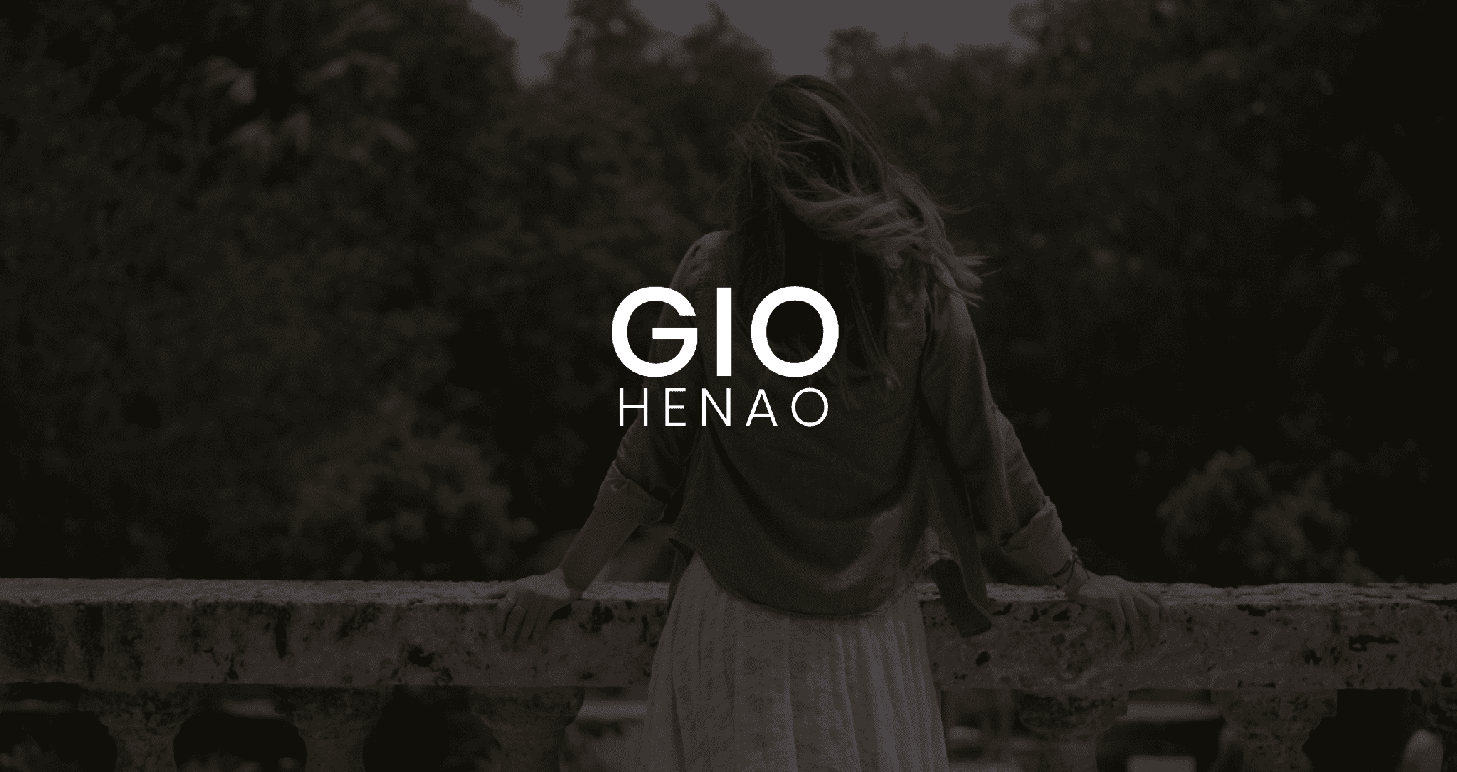 IU C&I Studios Page White Gio Henao Logo Featured Image with background with view from behind of Gio Henao leaning on a stone railing looking over a forest