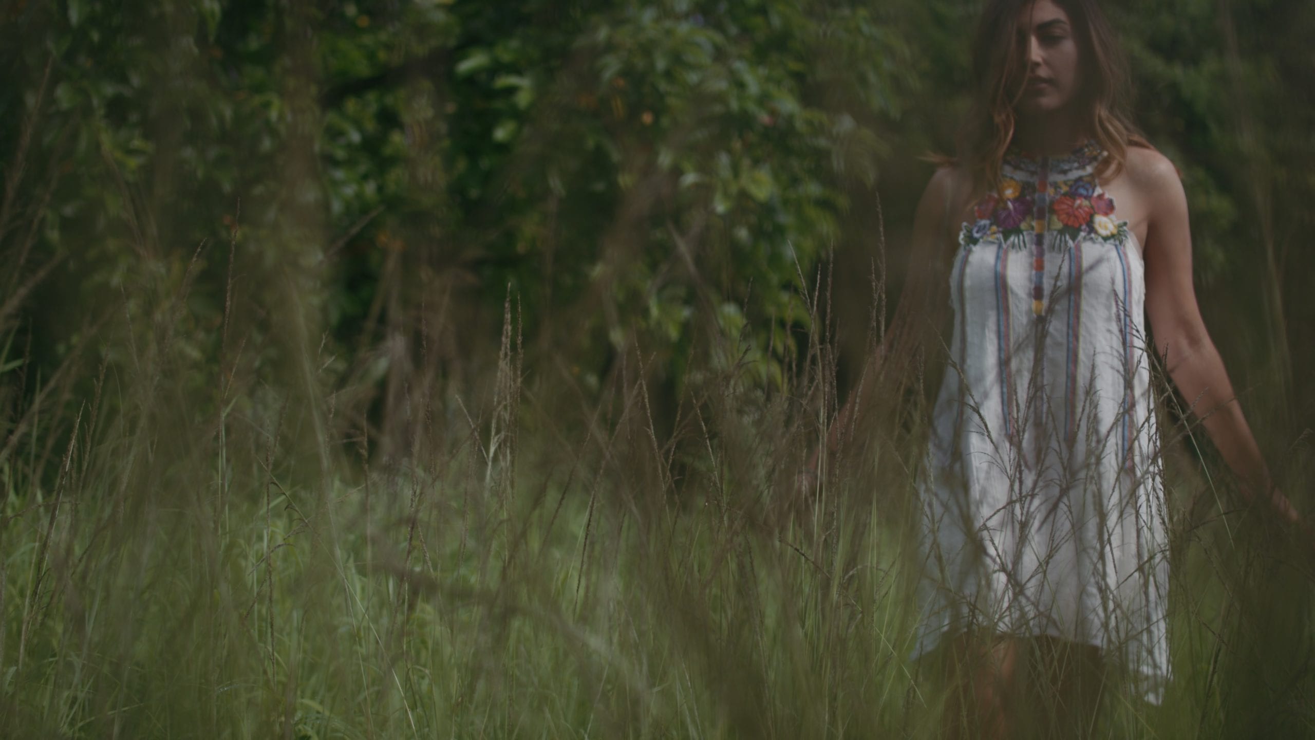 Gio Henao posing for the camera wearing a dress standing in tall weeds