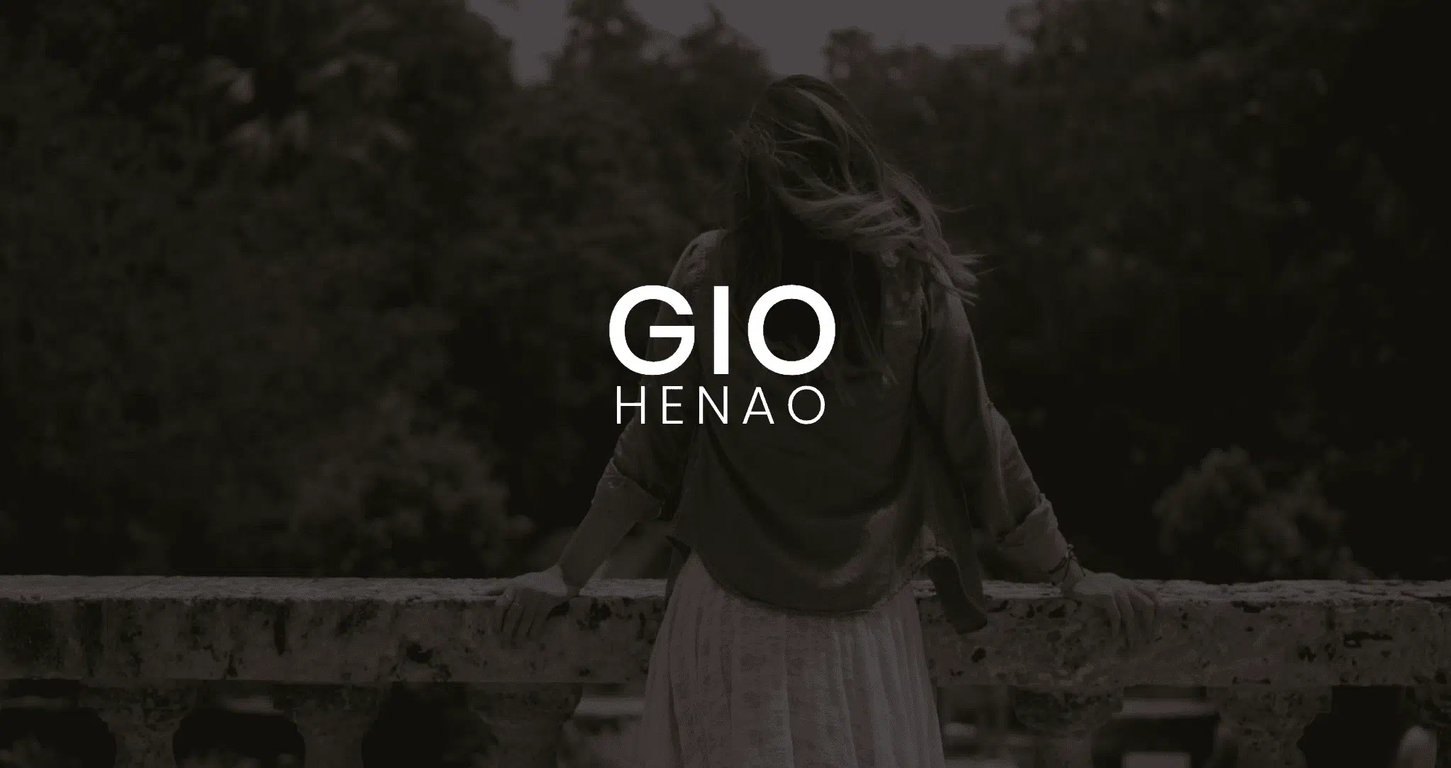 IU C&I Studios Page White Gio Henao Logo Featured Image with background with view from behind of Gio Henao leaning on a stone railing looking over a forest
