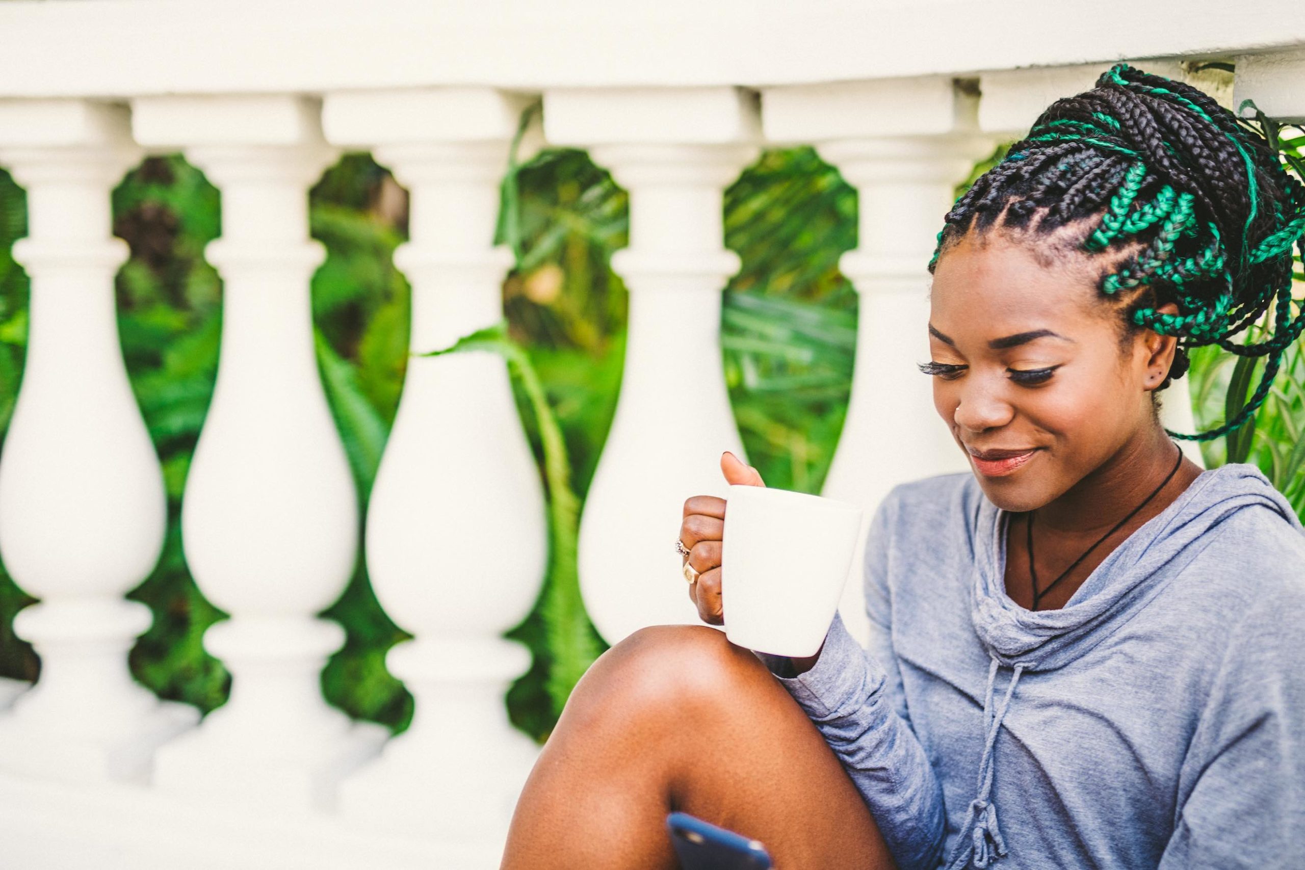 African American woman with black and green dreads enjoying a white cup of coffee on a patio