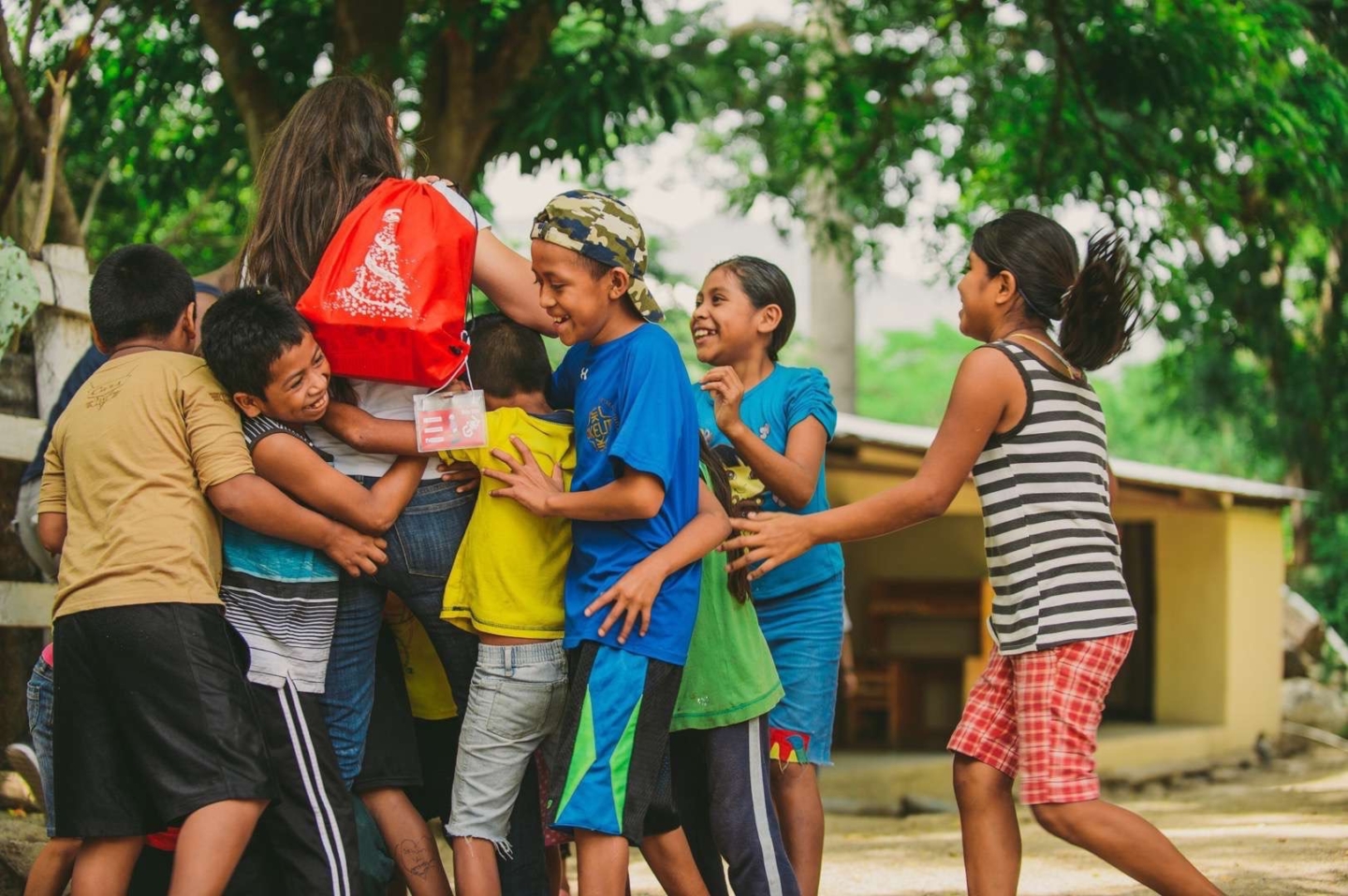 Group of children surrounding a female volunteer holding a red bag