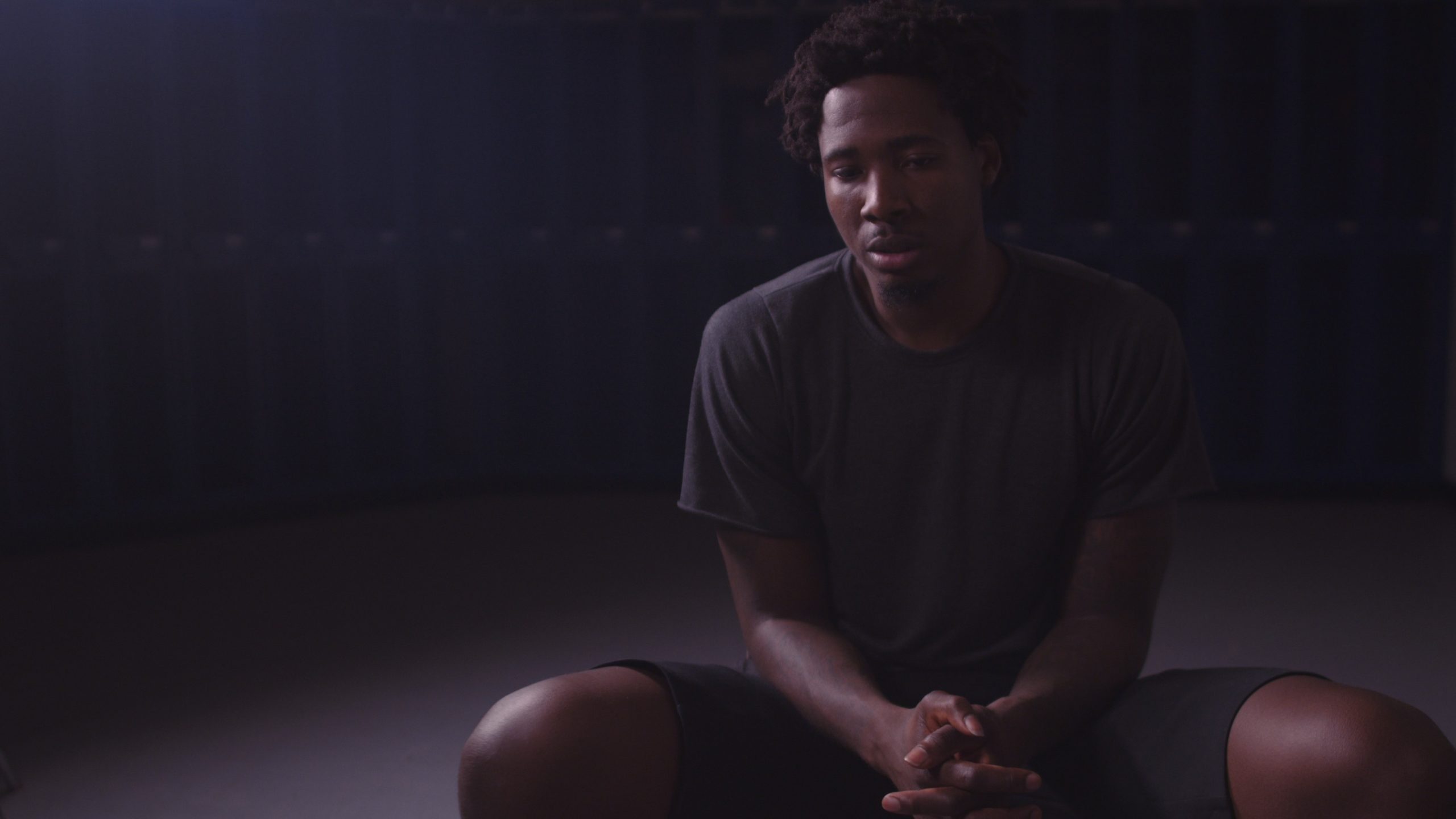 Ed Davis Sportsblog, a documentary mini series African American man wearing a gray t shirt and black shorts sitting and looking down