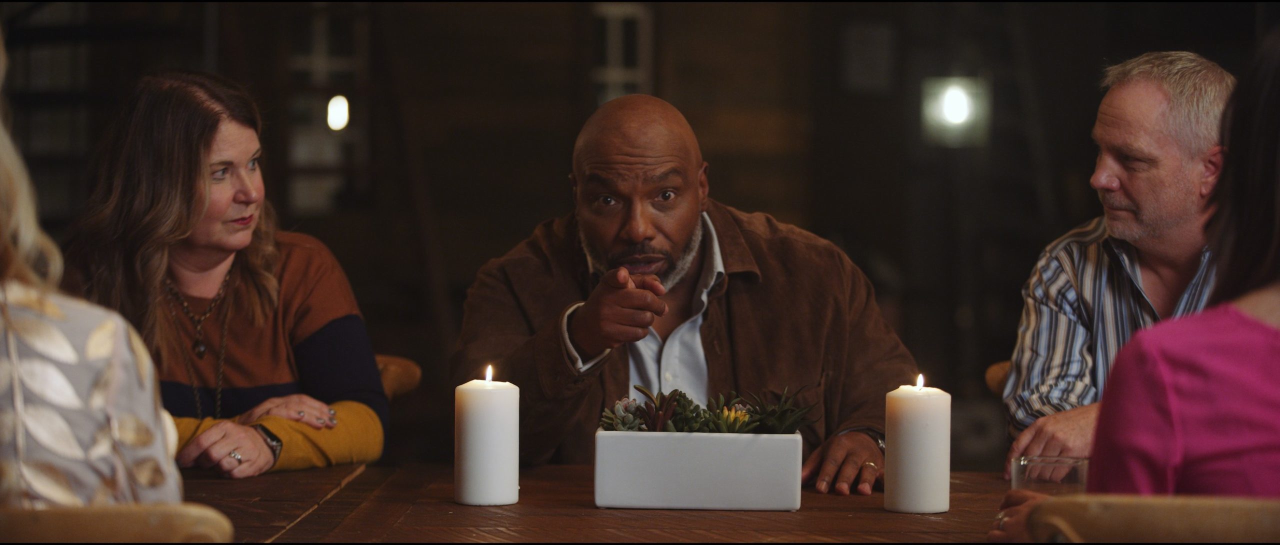 MRINetwork Company Video Lets Start Building African American man pointing finger at camera surrounded by a man and three women at a table with two white lit candles and small planter
