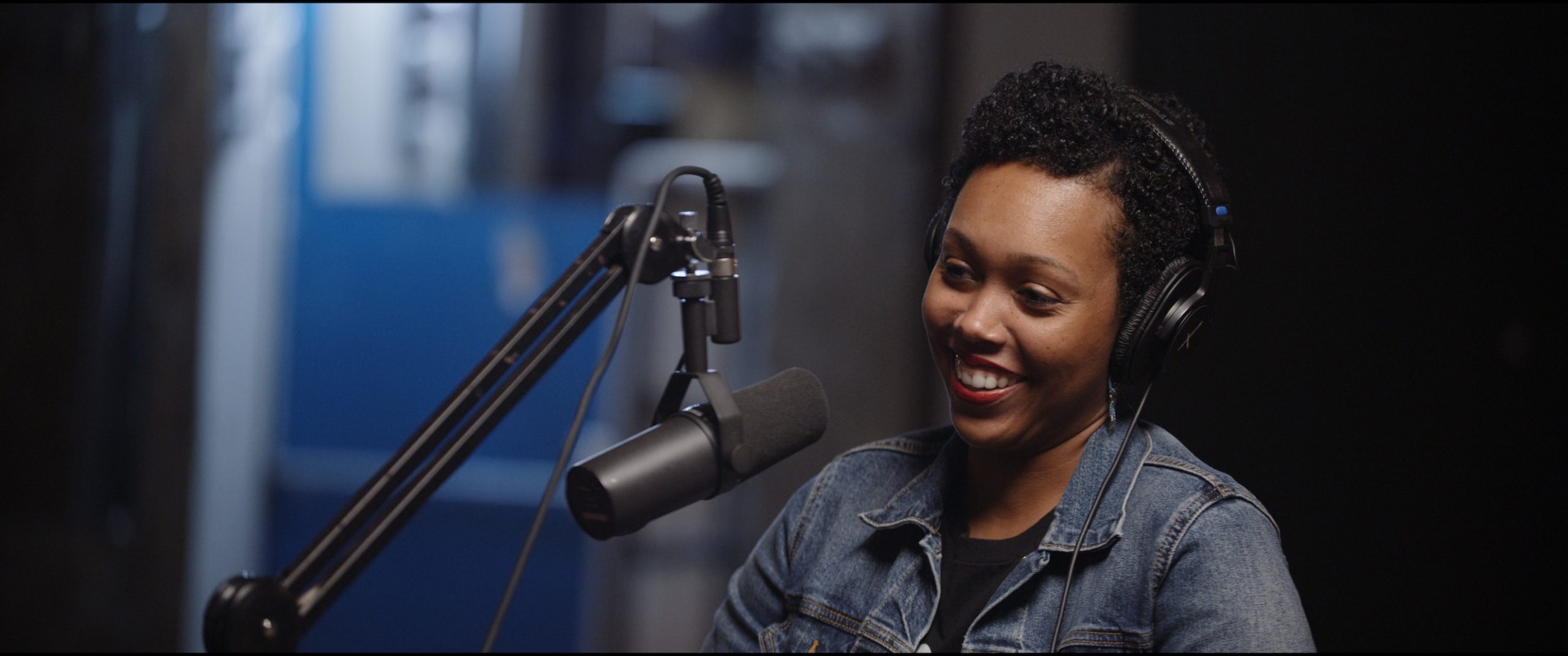 Season 2 of Uncreative Radio with Tiffany Lanier with her wearing headphones and smiling by a microphone