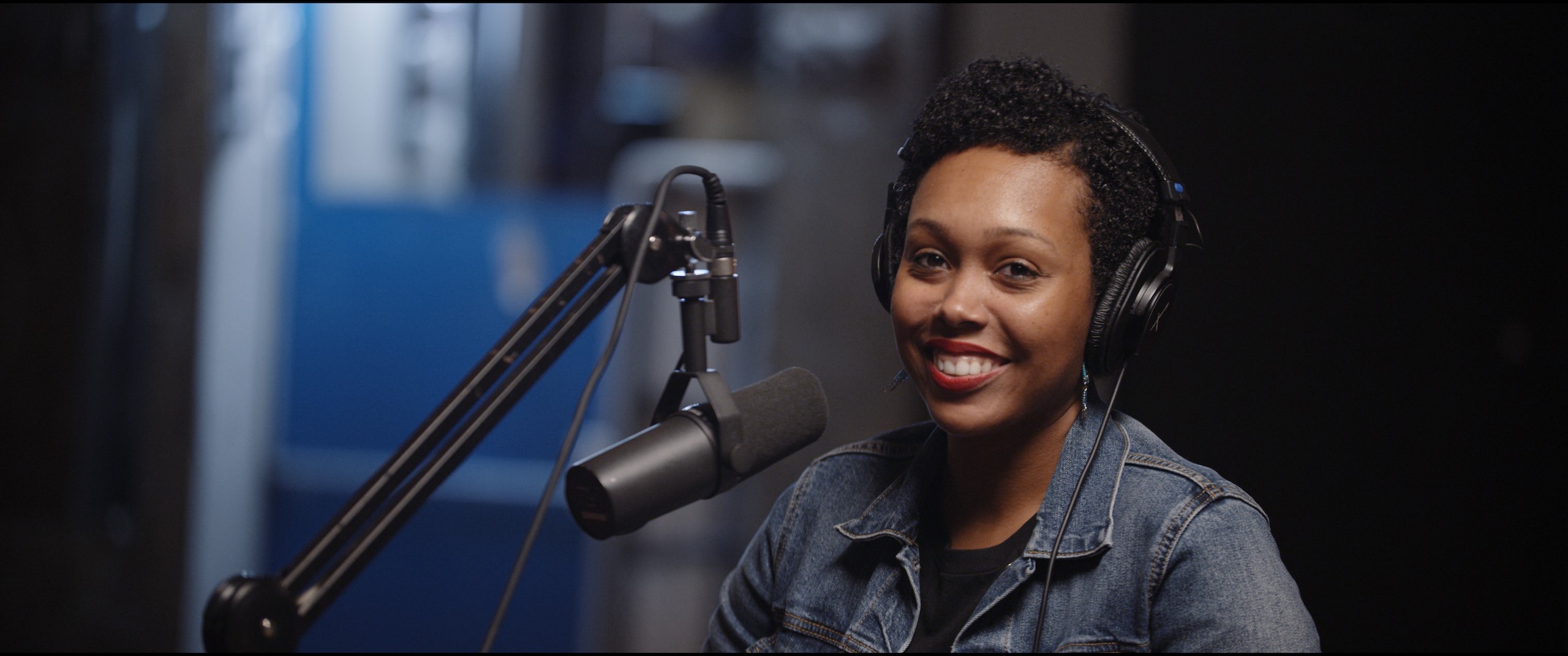 Season 2 of Uncreative Radio with Tiffany Lanier with her wearing headphones and smiling by a microphone posing for the camera