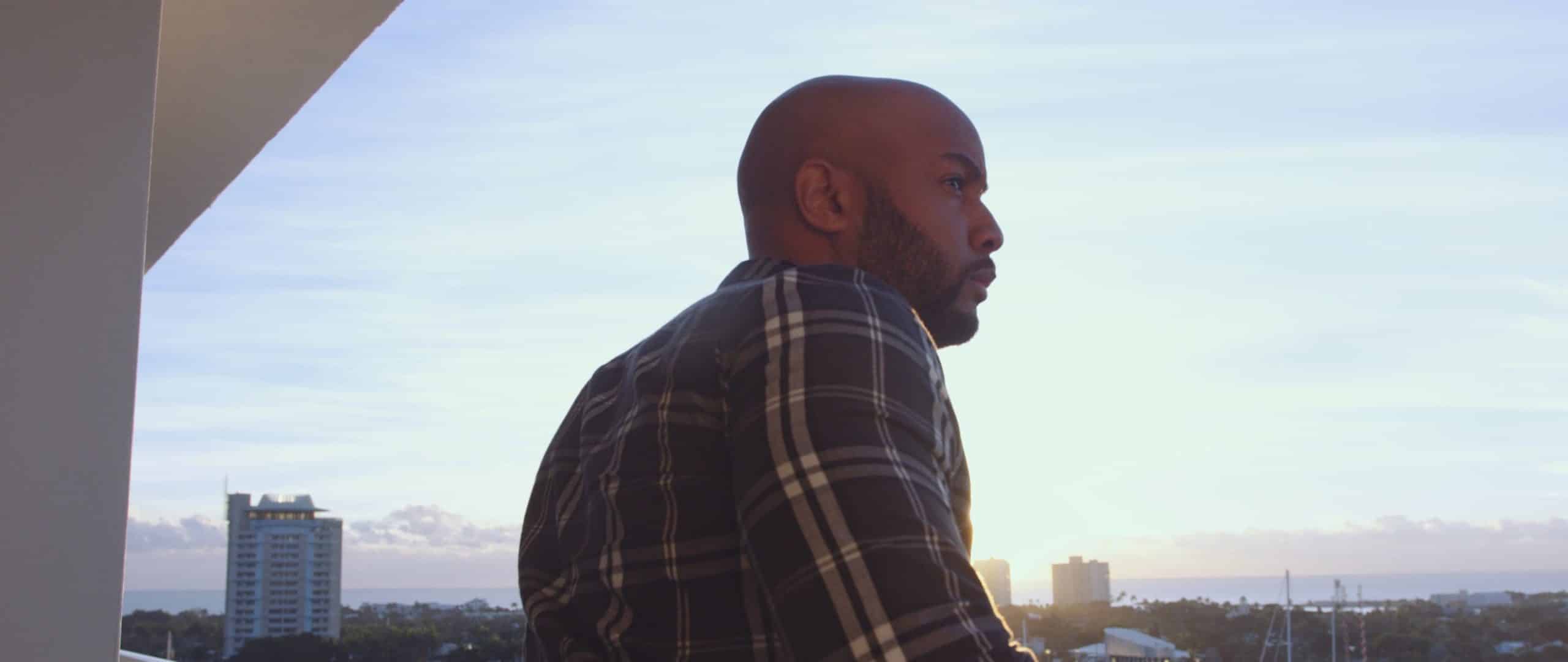 View from behind of an African American man looking out at the city from a balcony