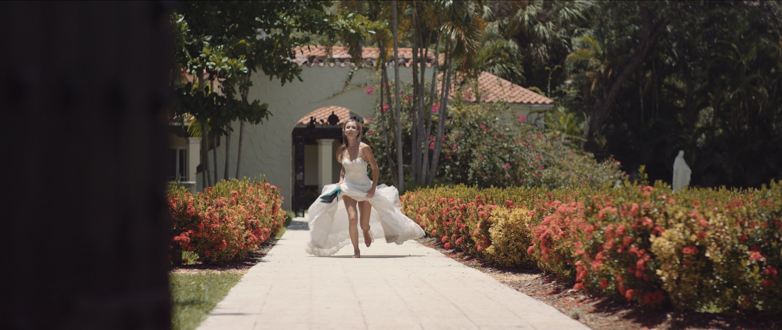 Dailies 0059 Delilah Castro Wedding Dresses Woman with long blond hair in white dress running down walkway holding her heels and hitching her dress up