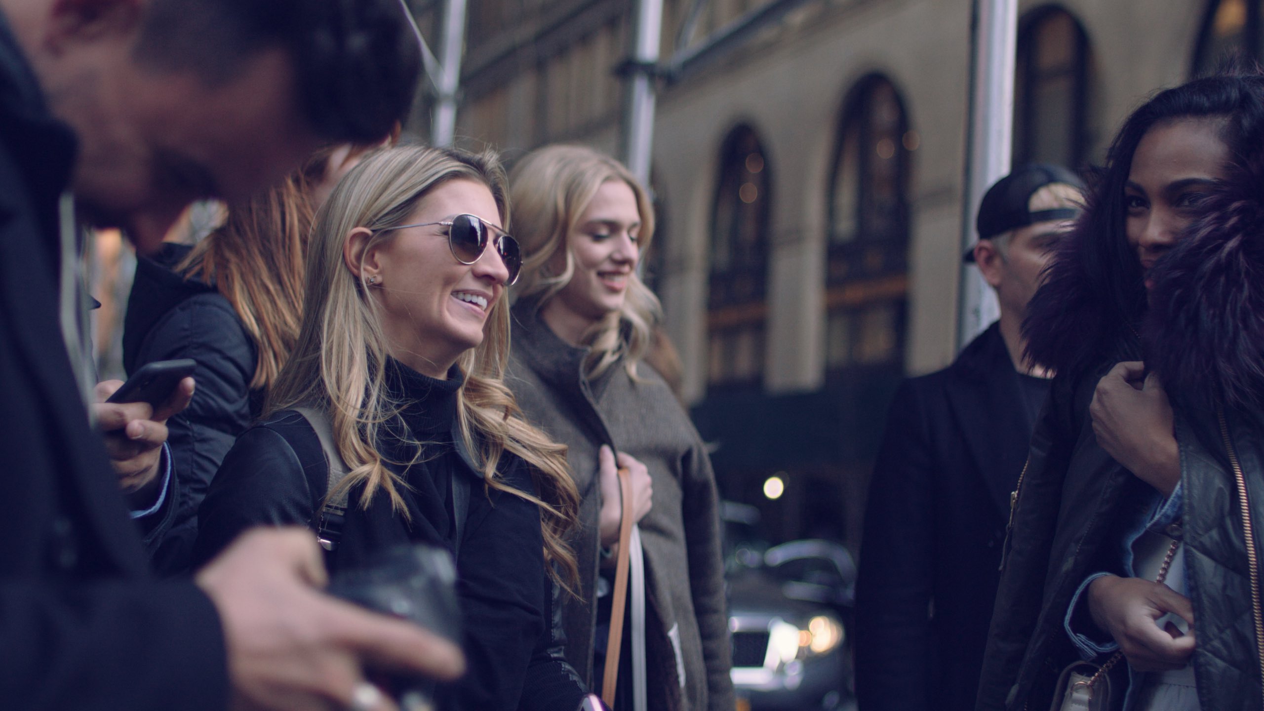 BTS Haute House Shoot Dailies 0058 Side profile of woman with long blond hair smiling in a crowd of people in a city