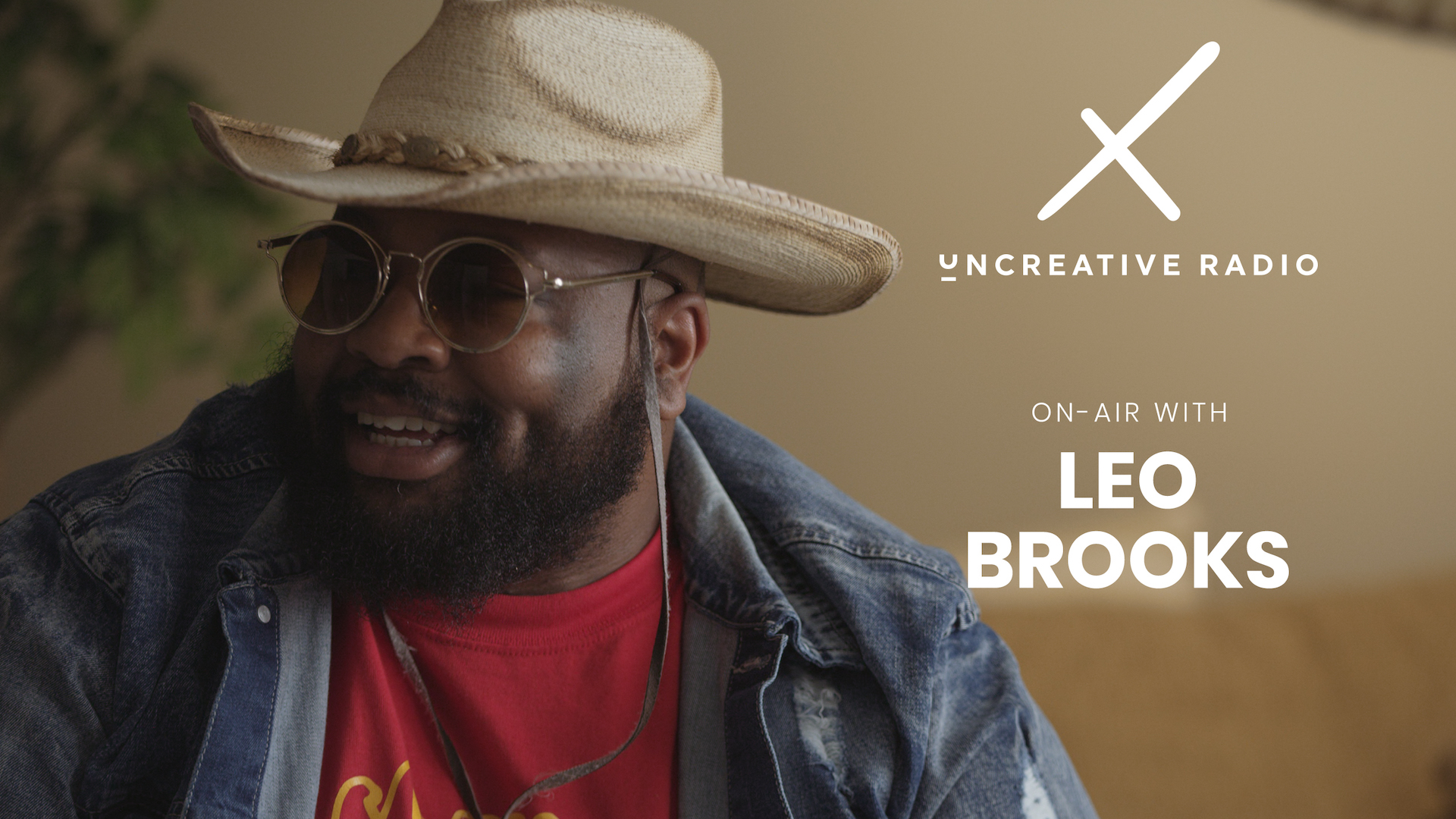 Uncreative Radio with Leo Brooks title with bearded man wearing shades and beige cowboy hat along with jean jacket and red t shirt smiling looking off to the side