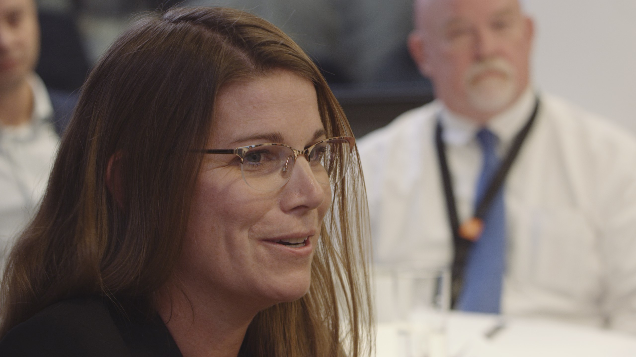 Stantec UK and NY Livestream International Live Streaming Event Closeup of woman with long brown hair wearing glasses talking with people in the background