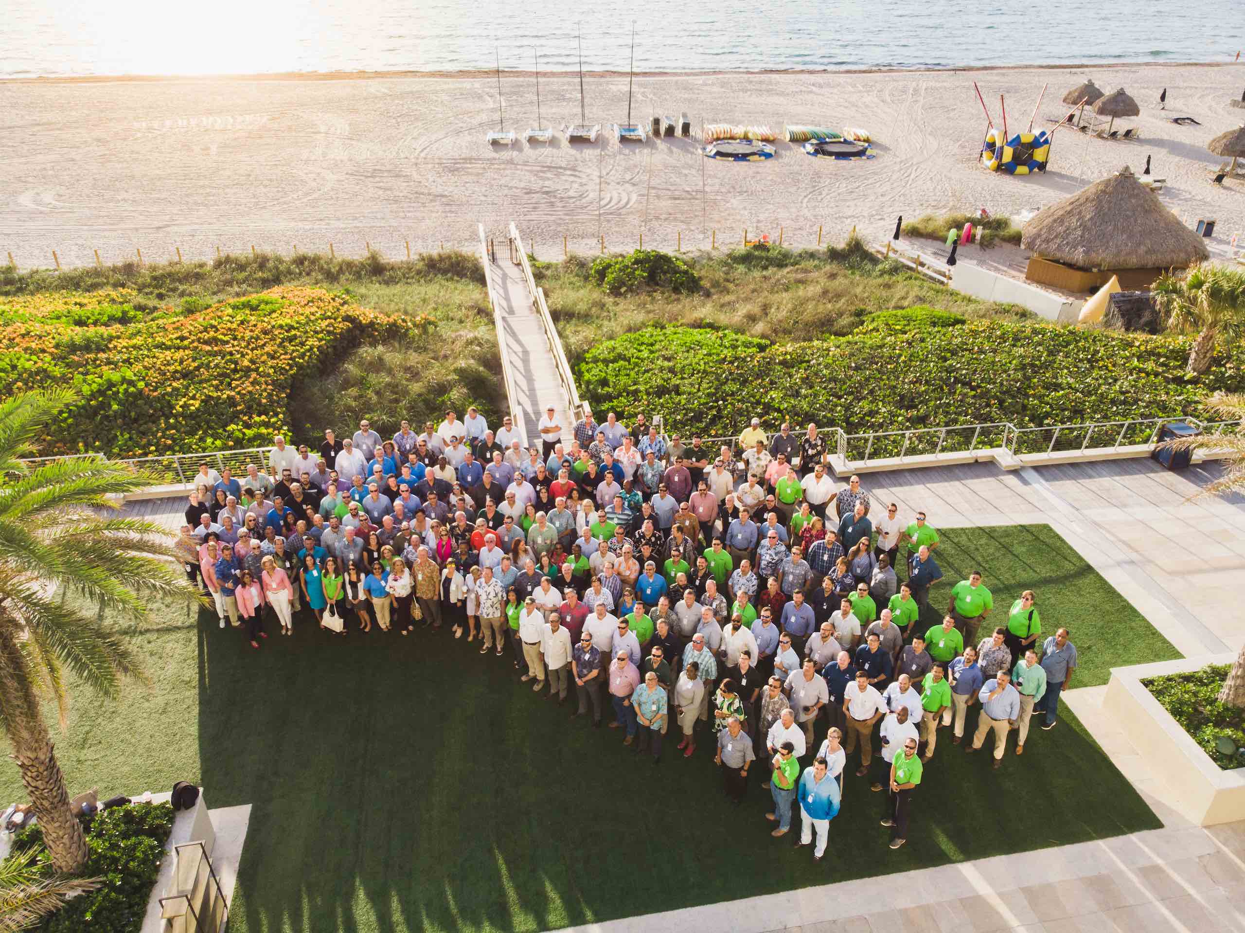 Moss Construction Fort Lauderdale Aerial view of group of people standing on green turf by a beach