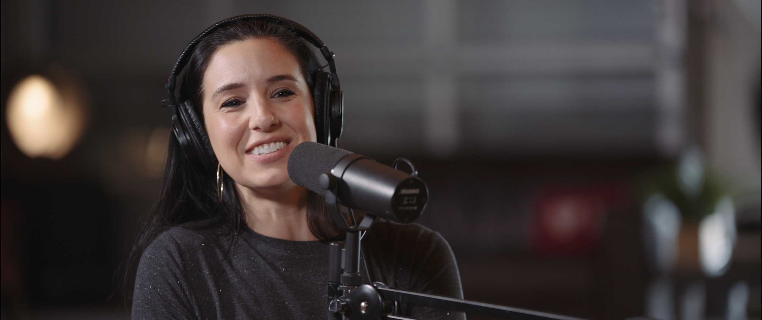 Uncreative Radio with Leslie Lynn Nifoussi wearing headphones and smiling by a microphone