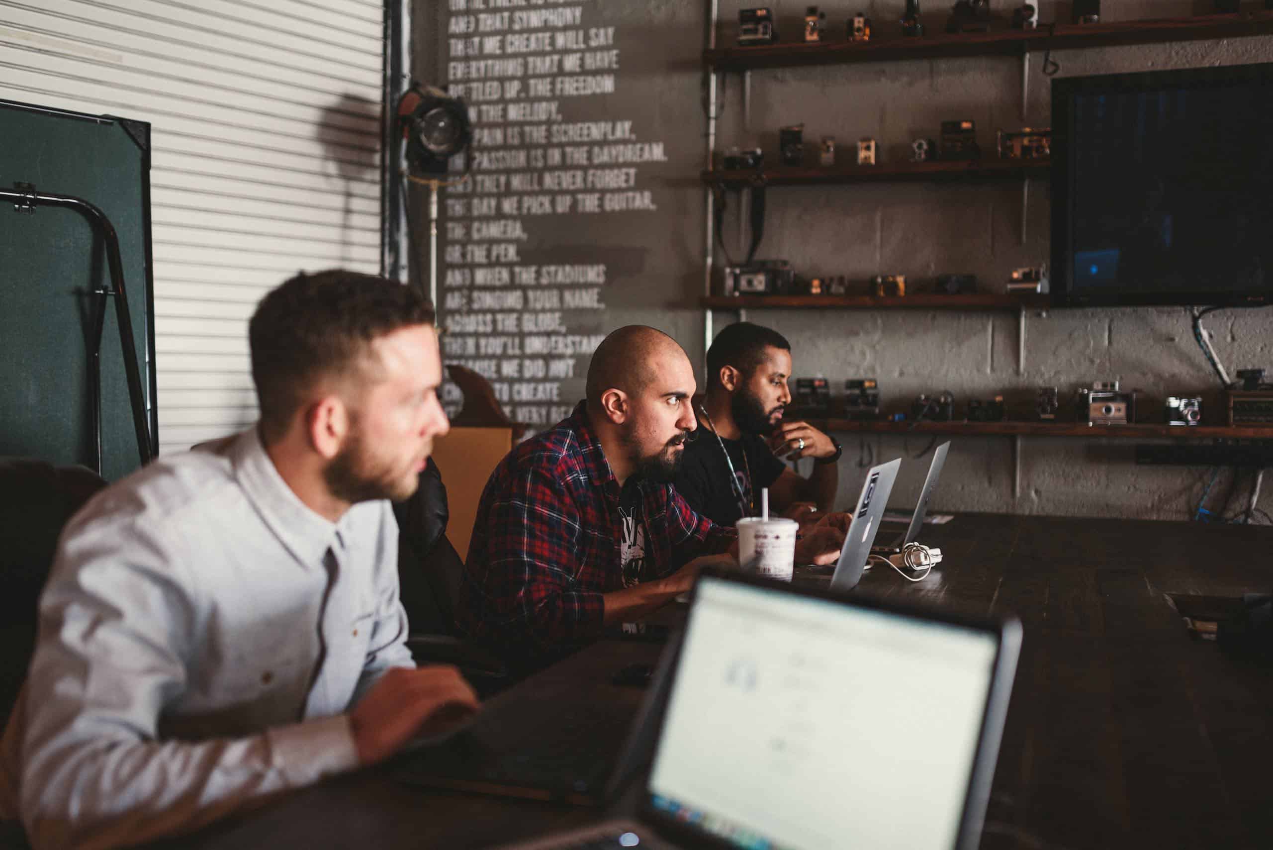 Three men sitting at a table with laptops