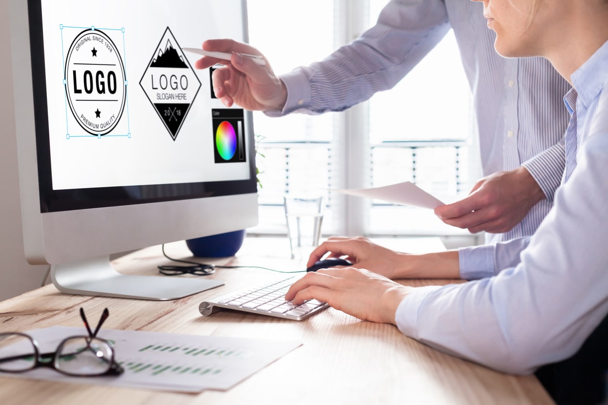 CTV Videos-Glasses, piece of paper and glass of water on table. Female and male working at the computer. Male is pointing to a logo icon on the screen while female is using a mouse.