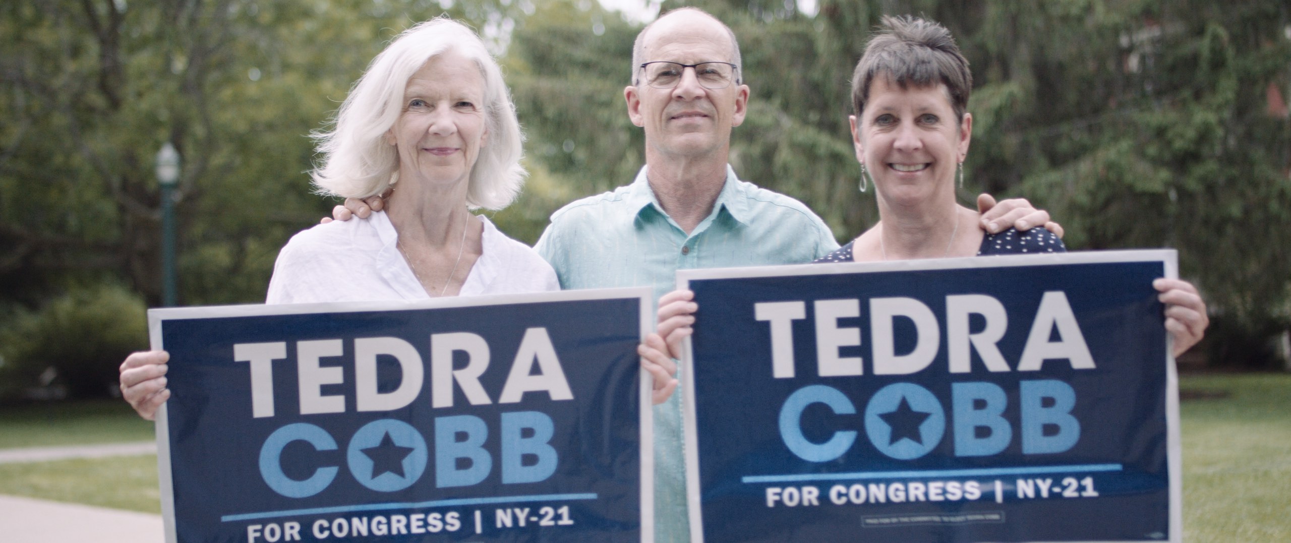 Dailies Political season with 76 Words Man in light blue shirt between two women holding Tedra Cobb for Congress NY 21 signs