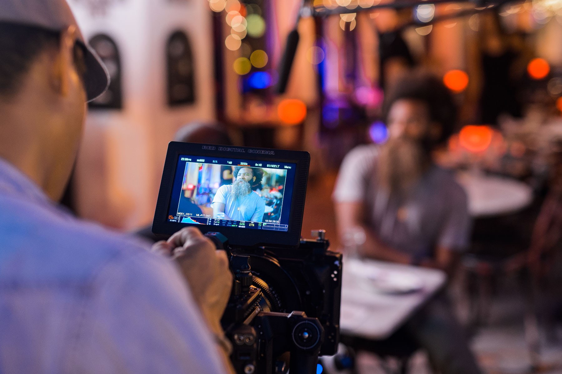 Love and War Feature film mastering and delivery services by C&I Studios View from behind of crew member looking at video display of man with bushy beard sitting at table in a restaurant
